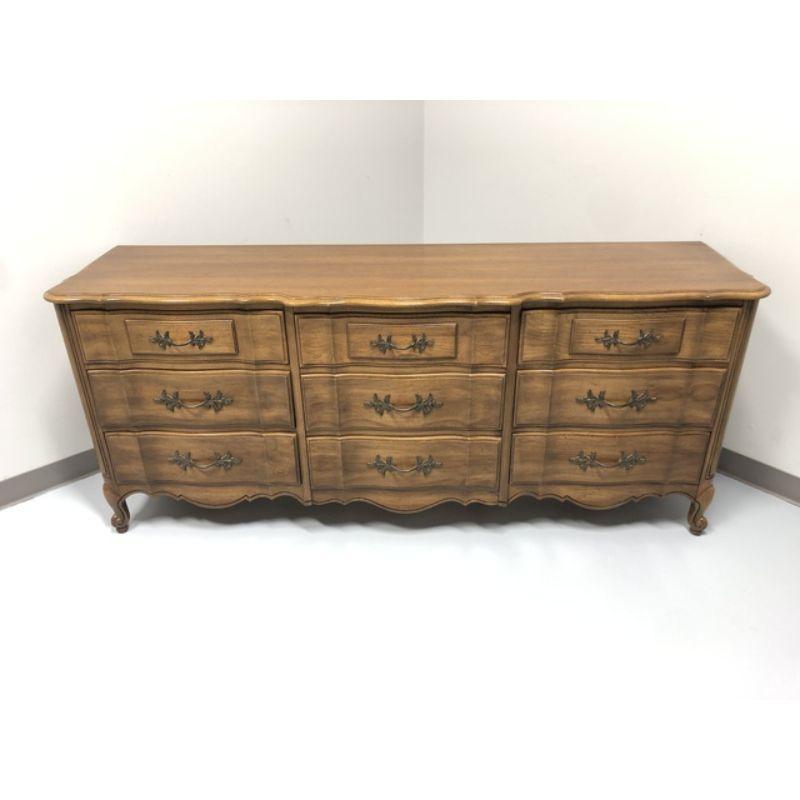 French Country style Triple Nine Drawer dresser by quality furniture maker Thomasville. Made in North Carolina, USA in the Mid to Late 20th Century. Made from oak with brass hardware. Dovetail construction. The curvy serpentine front, scroll feet,