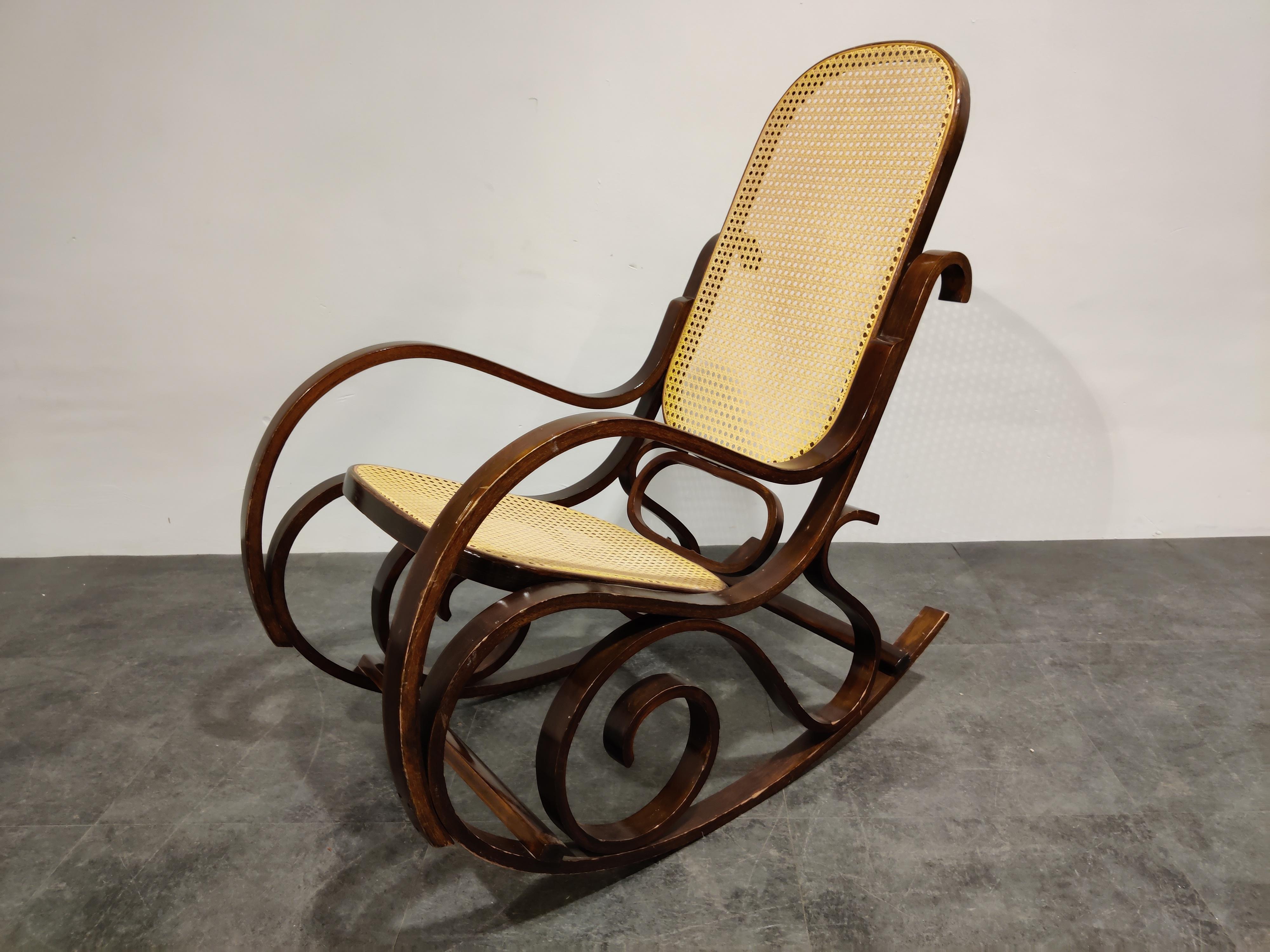 Midcentury dark brown wooden and cane webbing rocking chair.

These Thonet style rocking chair has a very elegant curling shape and look and are ideal to create a contrast in your interior.

Good condition with minor wear.

Cane seats and