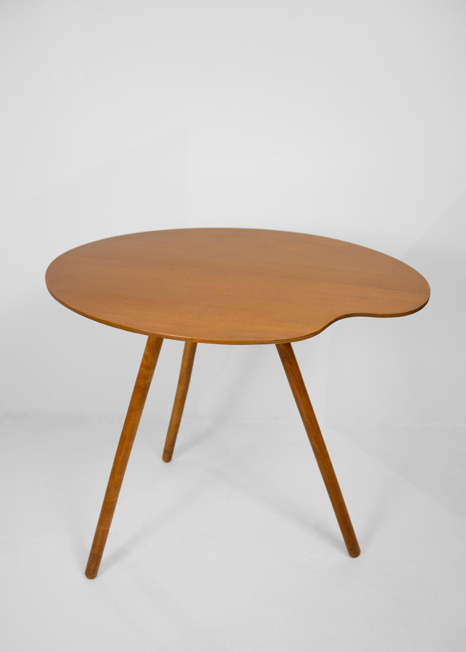 Ein dreibeiniger, handwerklich gefertigter Beistelltisch aus Holz mit Farbpalette, der natürliche Formen und Materialien enthält. Das verspielte Design verleiht diesem vielseitigen Stück eine skurrile Note.