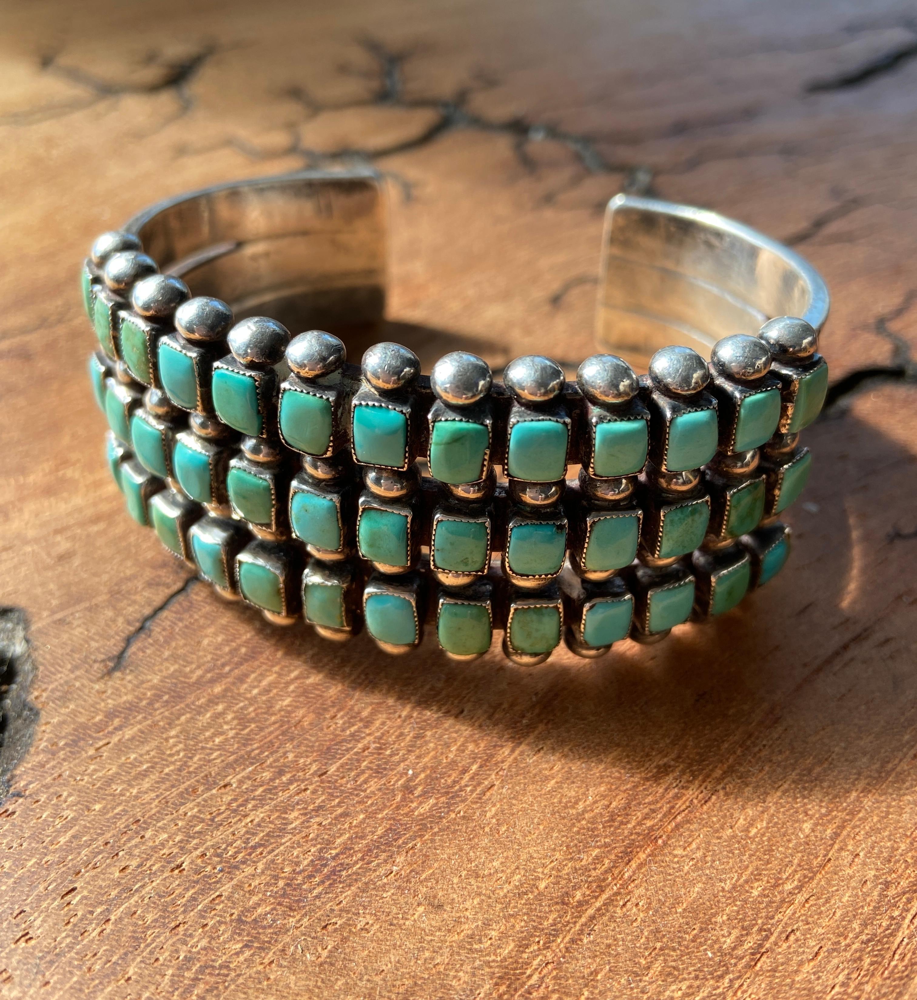 Questo braccialetto vintage fatto a mano, ispirato agli indiani Zuni del sud-ovest, è stato creato con argento sterling e pietre di turchese cabochon multicolore. Il corpo del bracciale è composto da tre strisce martellate che si assottigliano.  da