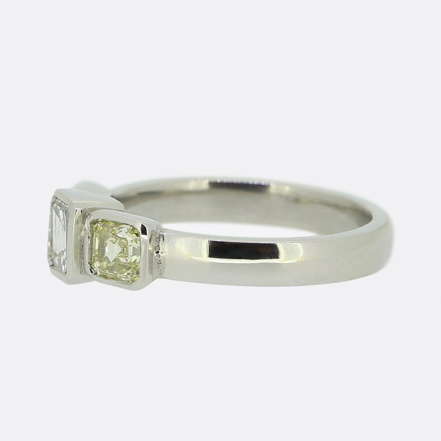 Here we have a fabulous three-stone diamond ring. At the centre sits a bright white asscher cut diamond in a flush rub-over setting. This proud principle stone is then flanked on either side by a single antique fancy yellow asscher cut diamond in a