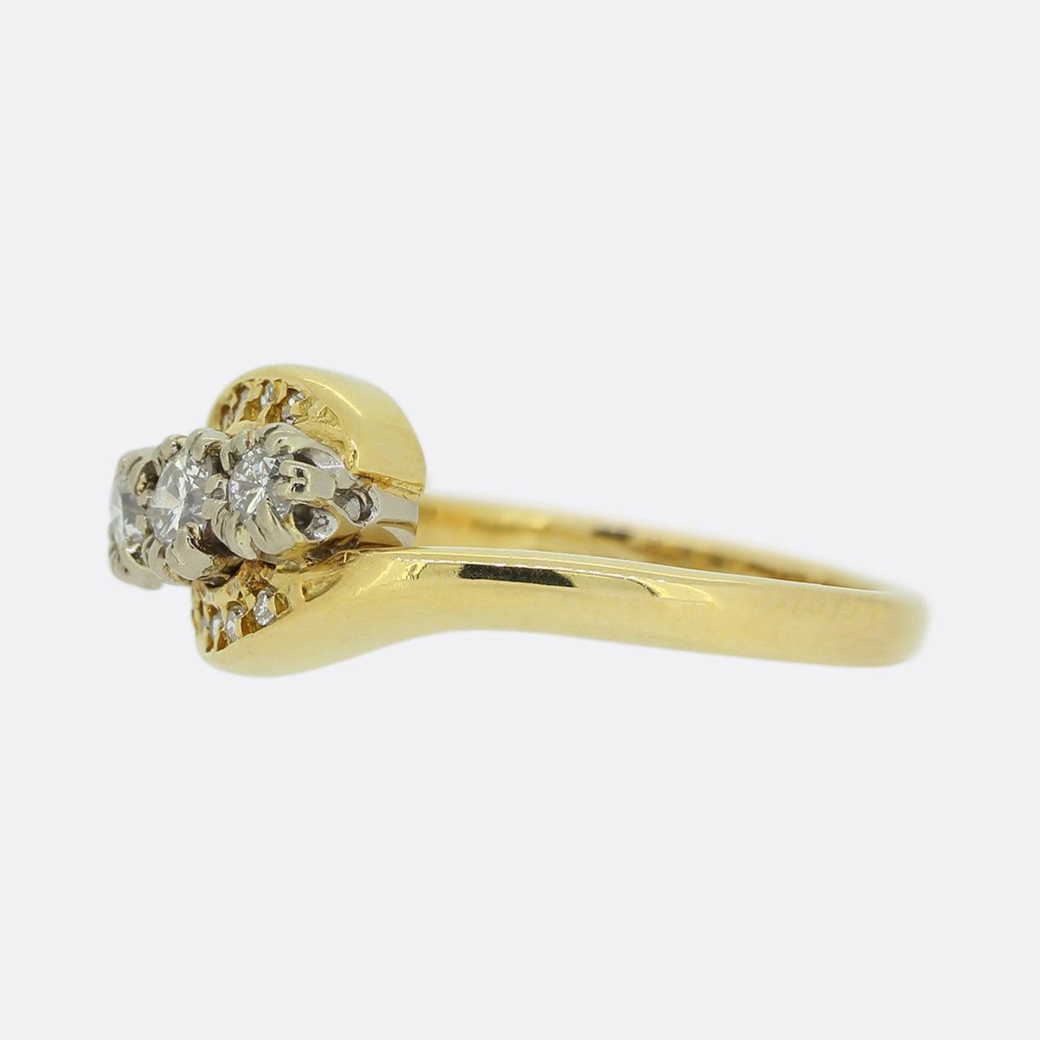 This is a vintage three stone diamond ring. Crafted from 18ct yellow gold, this piece showcases three diagonally claw set round brilliant cut diamonds. These focal stones sit slightly risen upon a swirling face where we find an additional eight