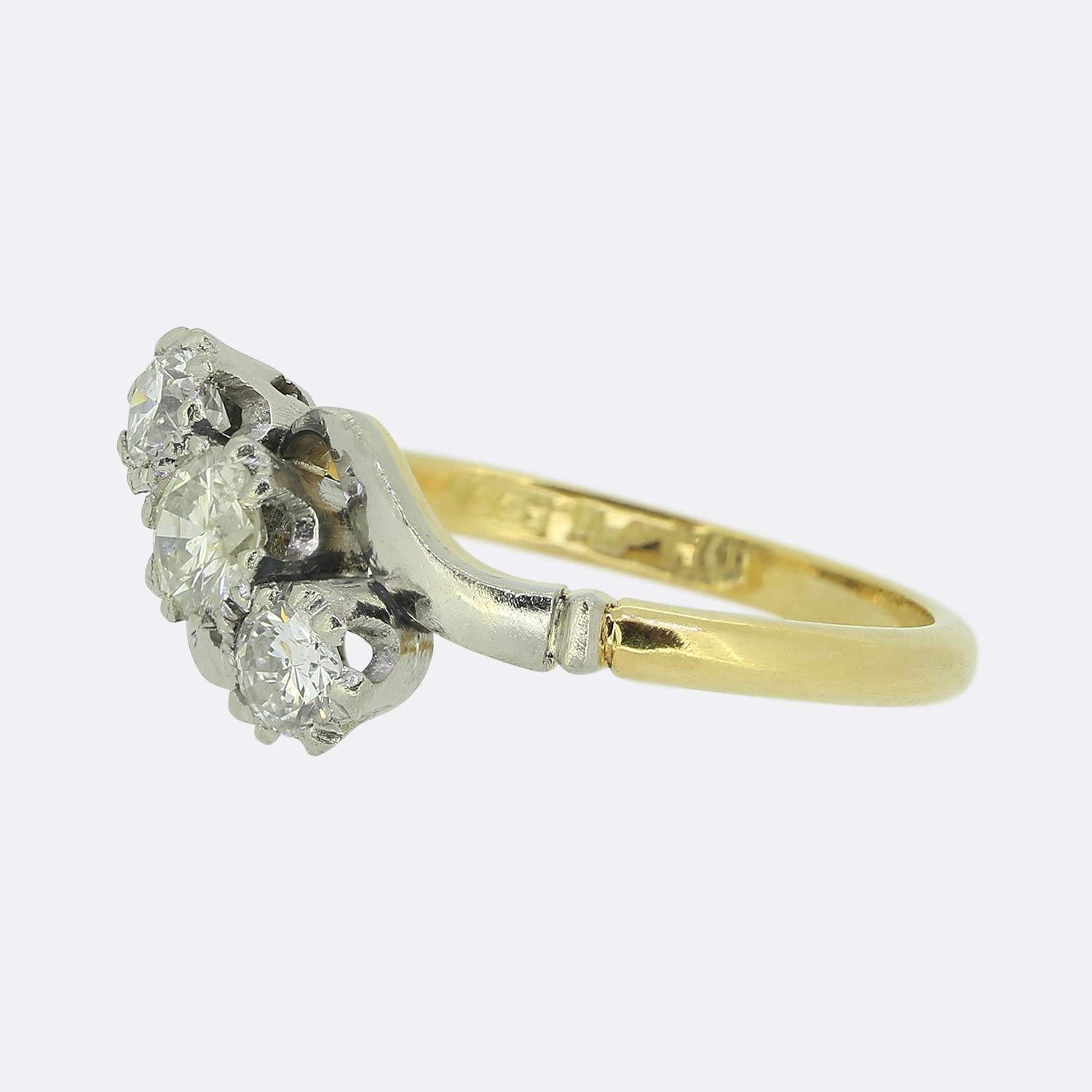 Aquí tenemos un anillo remolino de diamantes vintage de tres piedras. Un trío de diamantes redondos facetados se han engastado individualmente en garras de platino en una formación diagonal colectiva a lo largo de la cara. Estas tres piedras se
