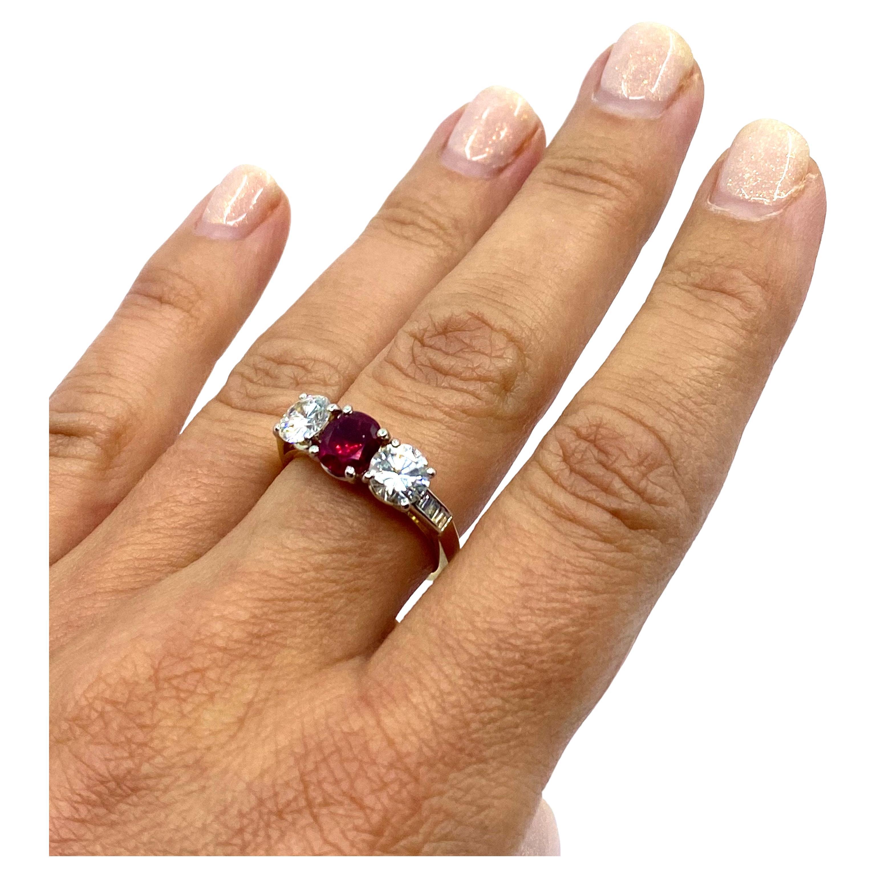 

A beautiful three stone engagement ring, made of 18k gold, featuring diamonds and a ruby.
The oval cut ruby is set in the center and surrounded by two brilliant cut diamonds. Baguette cut diamonds flank the central stones and adorn the shank. All