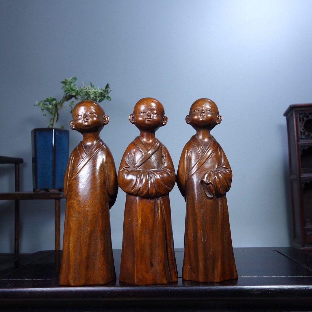 Three beautiful hand carved wood monks with smiles. The monks stands with their eyes looking up. Their faces with full, rosy cheeks and delicate features in small mouths with cherry colored lips and thin arched brows, all set in a gentle, smiling