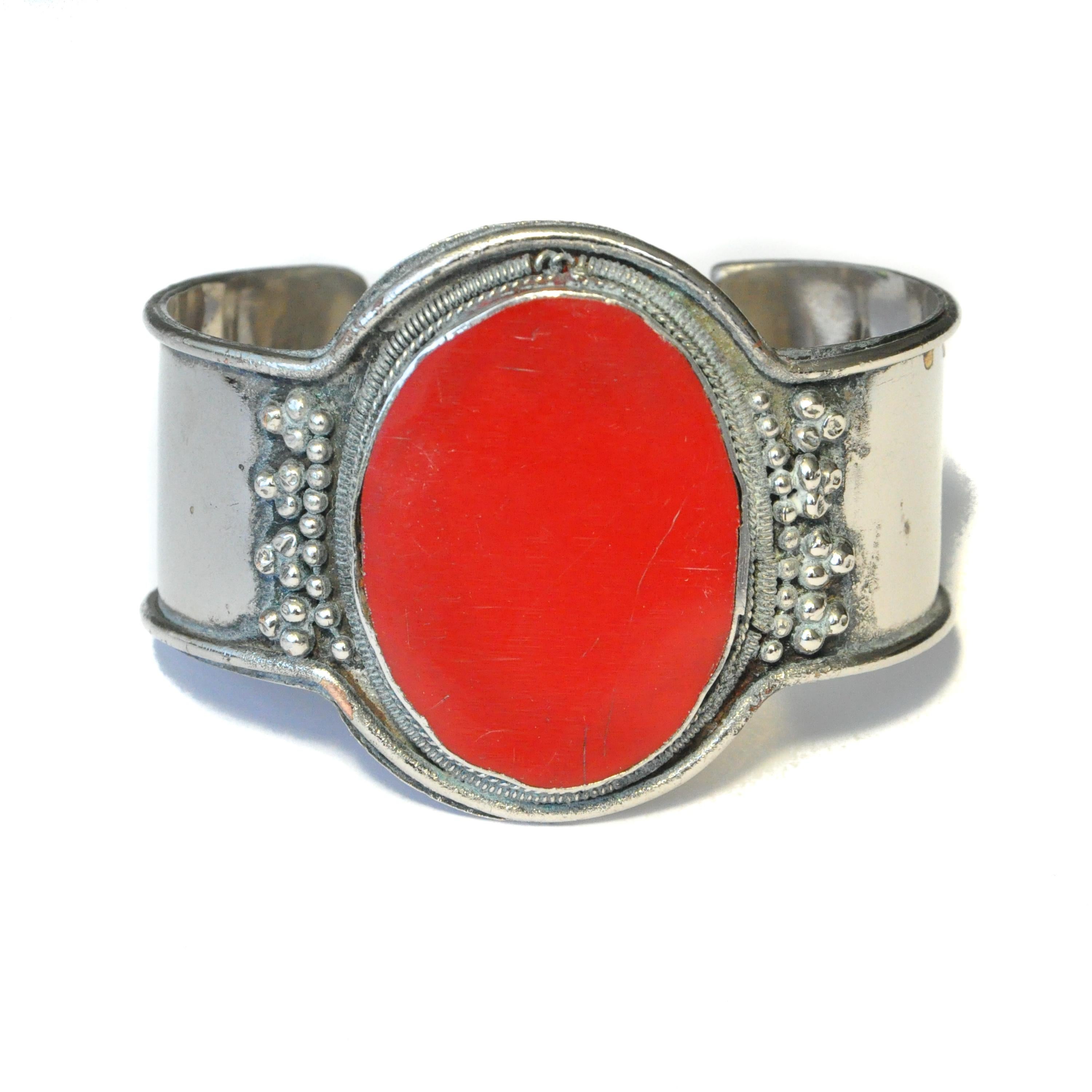 A Tibetan ethnic-style bracelet made of silver that has been fashioned into a solid silver bangle. The front of the bangle features a very large, oval chunky red stone that has been vertical inlaid. The silver has an upraised edge, at the front side