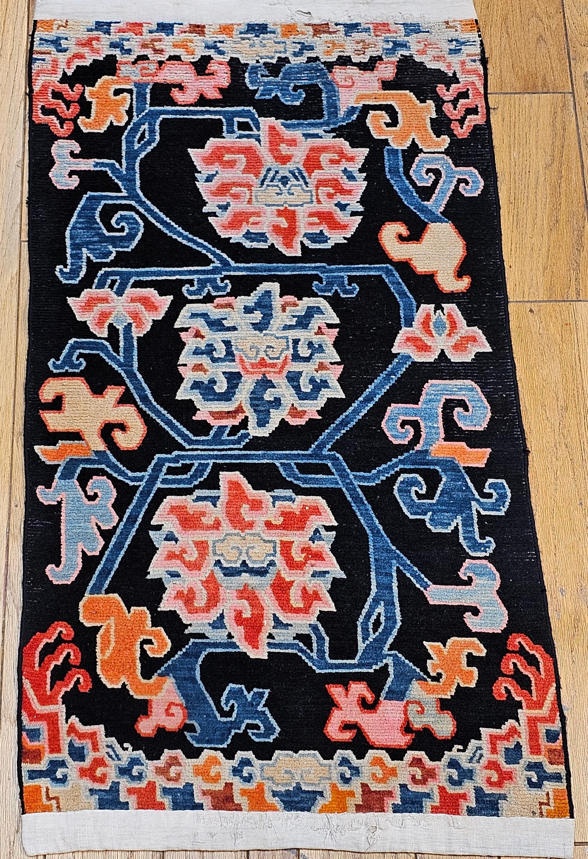 Vintage Tibetan Rug with Lotus Flowers and Cloud Symbols in French Blue and Red from the early 1900s.  Its field is designed with three large-scale Lotus flowers with protruding vines set on a black background color which creates color contrast