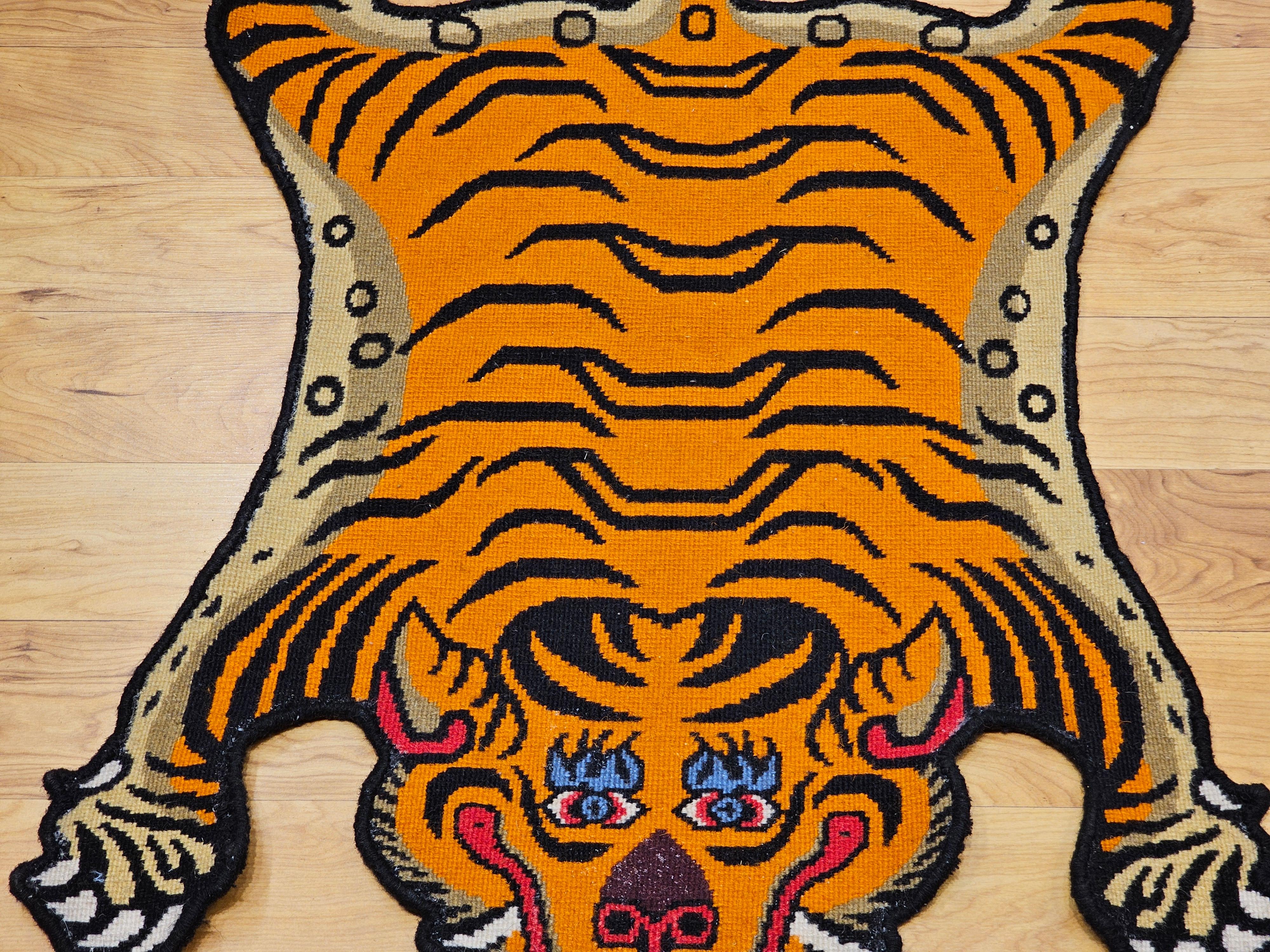 Tibetischer Vintage-Teppich in Tigerform in Orange, Schwarz, Rot und Blau.  Der Teppich hat die Form eines Tigerfells, das sich flach auf den Boden legt.  Die Grundfarbe ist leuchtend orange mit schwarzer Zeichnung.  Der Teppich kann auf dem Boden