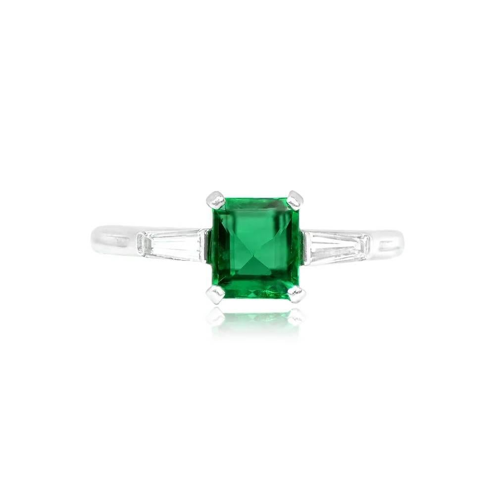 This vintage Tiffany ring showcases a vibrant Colombian emerald cut emerald with enchanting green saturation. Accentuating the center stone, two tapered baguette diamonds elegantly flank it, contributing to the ring's timeless allure. The total