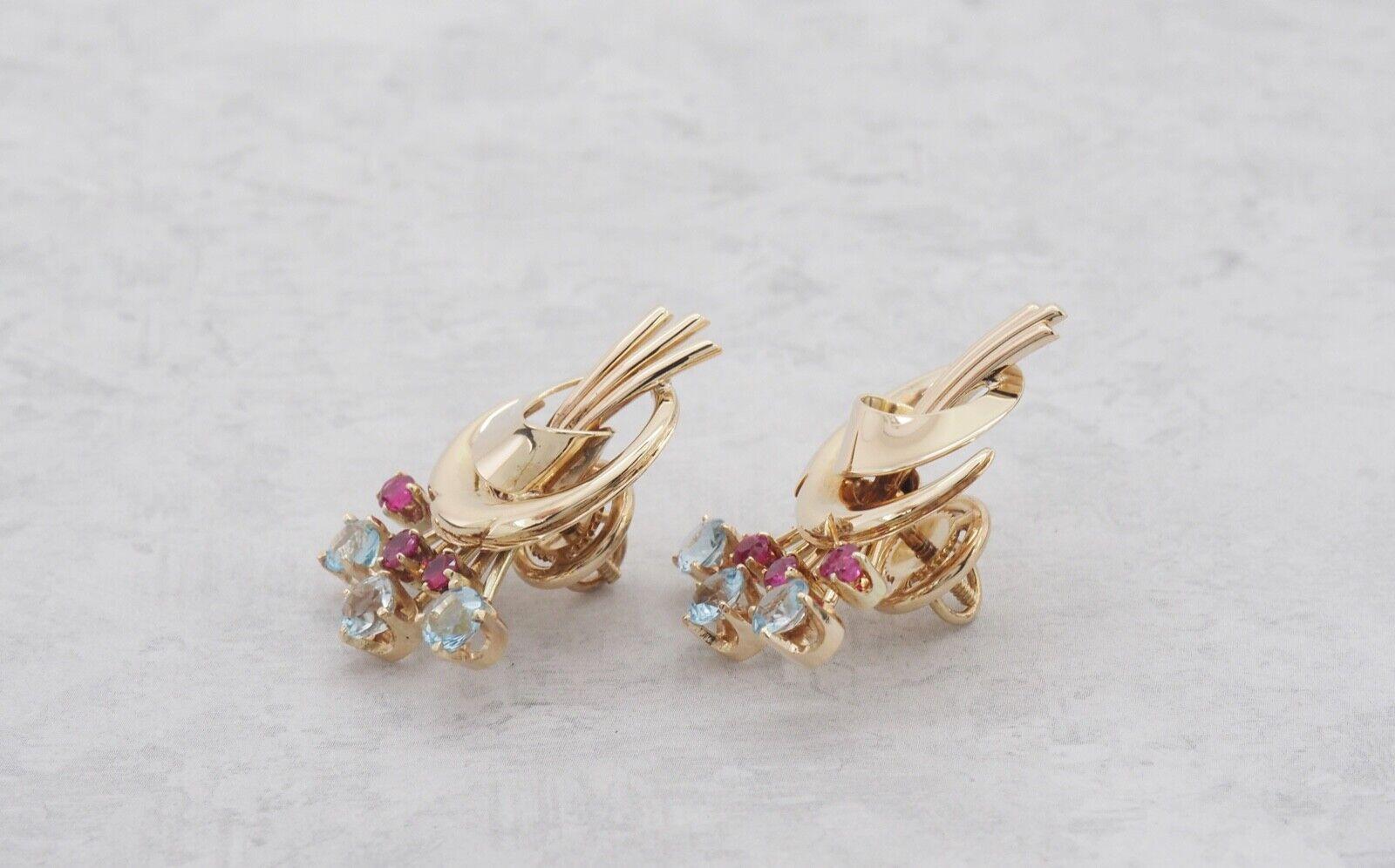 Diese atemberaubenden Ohrringe aus 14-karätigem Gold von Tiffany & Co. verkörpern mit ihrem skulpturalen Bandmotiv und den lebhaften Edelsteinakzenten die Eleganz der Jahrhundertmitte. Die in Zacken gefassten blauen Topase und Rubine in einem