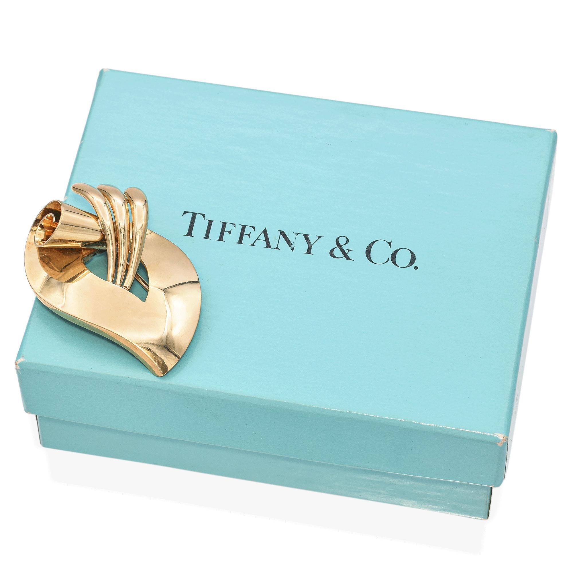 This elegant 14K gold brooch by Tiffany & Co. showcases a striking retro design. The piece features a bold, abstract form with smooth, flowing curves and a polished finish.
The brooch is crafted with a dynamic interplay of geometrical shapes,