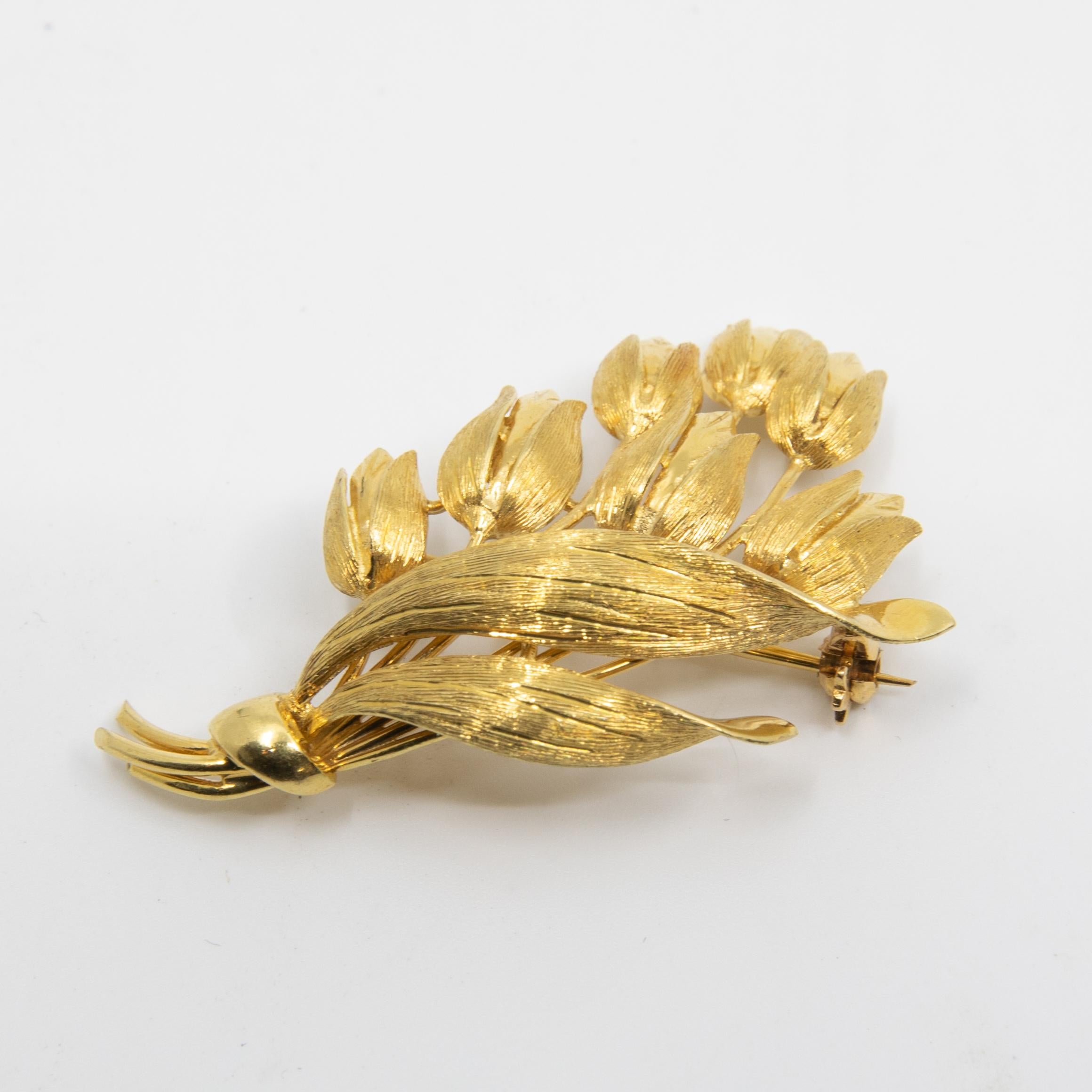 Offered is a lovely authentic vintage brooch from Tiffany & Co. It is crafted from solid 18k yellow gold with a fine polished finish and features a bunch of tulip flowers with leaves tied at the end to form a bouquet. It has the safety clasp for the