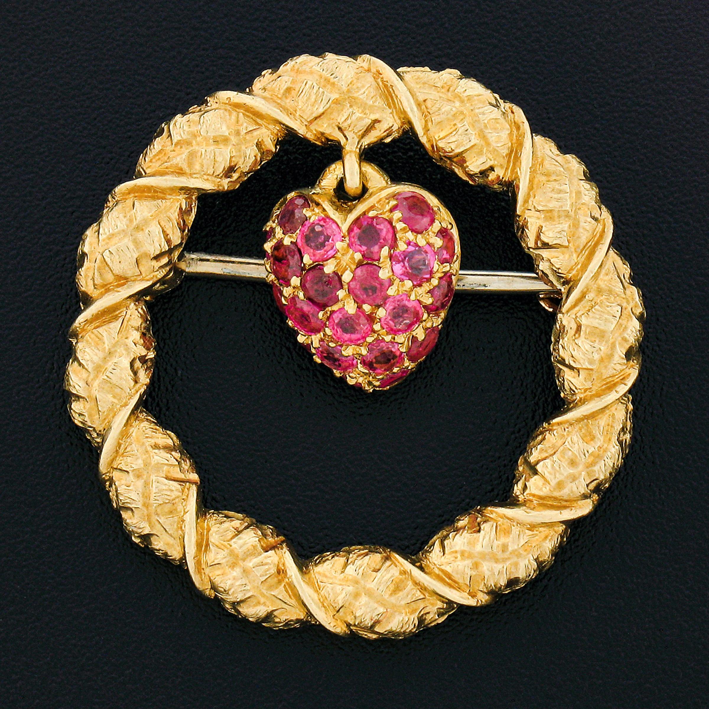 This wonderful vintage brooch by Tiffany & Co. is crafted in solid 18k yellow gold and features a truly elegant circle wreath design that is structured from uniquely textured gold throughout. A cute strawberry or heart ruby charm dangles from the