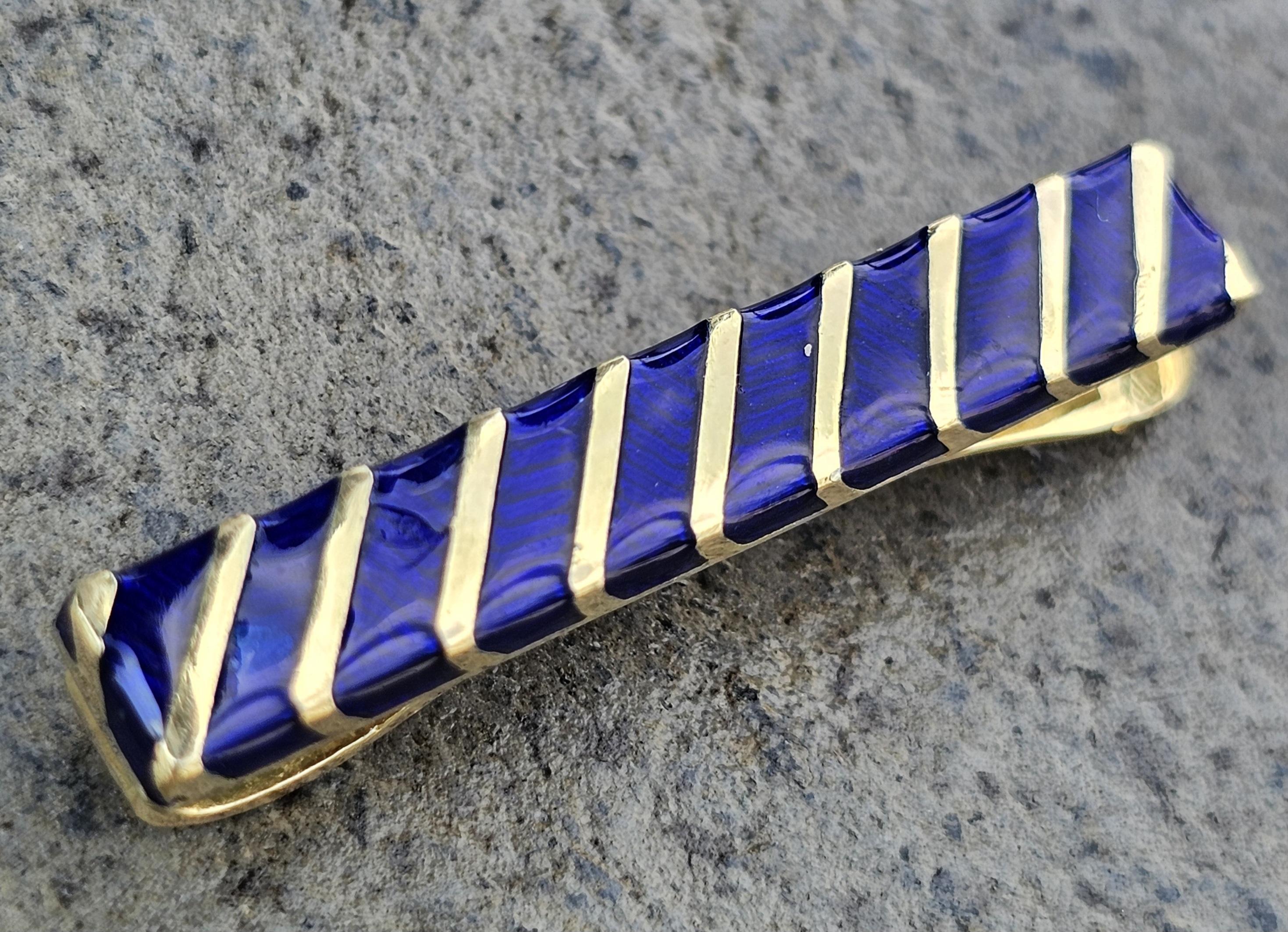 Arricchisci la tua collezione con questo raffinato fermacravatte di Tiffany & Co. Realizzato in oro giallo 18 carati e impreziosito da un ricco smalto blu, questo pezzo è una testimonianza di raffinata eleganza. Gli accenti dorati diagonali creano