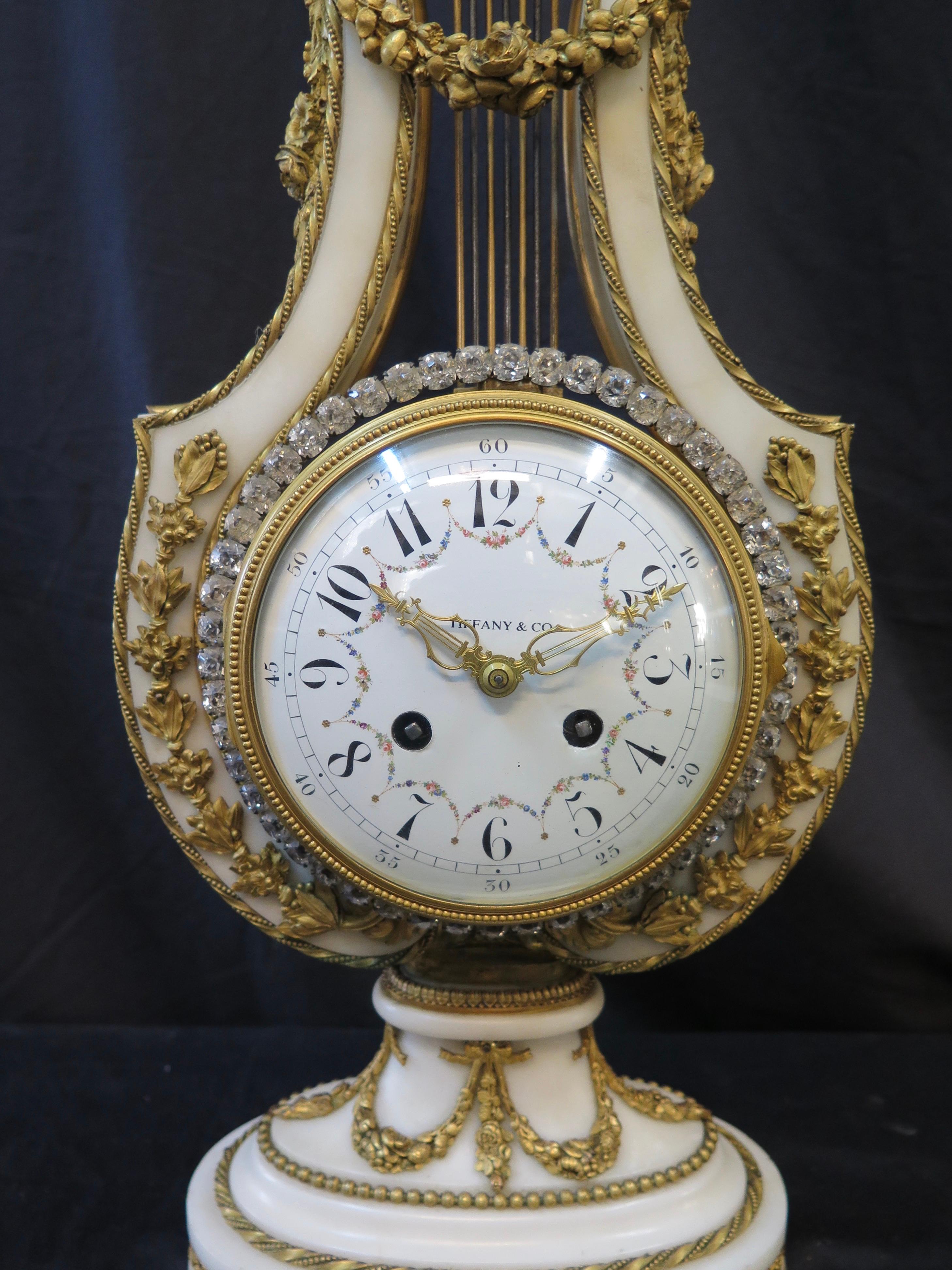 Tis stunning vintage 19th century French Empire white marble mantel (fireplace) clock was made for Tiffany & Co. The clock has a lyre shape body accented with doré' bronze sculpted embellishments of the period. The top of the clock features a