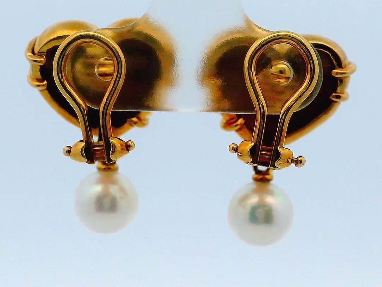 A striking pair of earrings, crafted in 18k gold by Tiffany & Co. in 1994. Each earring features a heart-shaped design adorned with delicate wrap-around details and a triangular accent. Suspended from the heart is a lustrous pearl drop.

Length:
