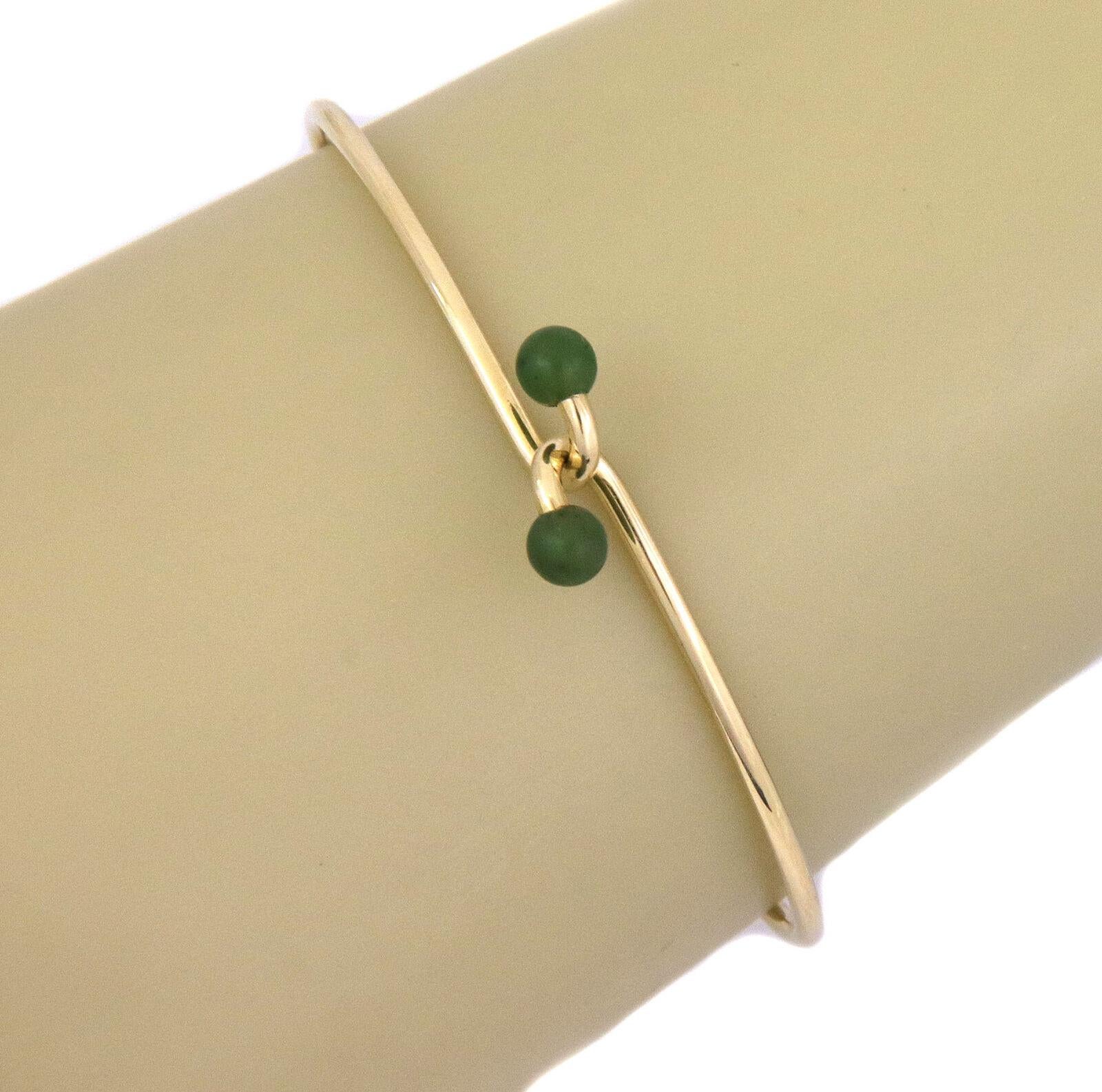 This is an elegant authentic bangle from Tiffany & Co. It is crafted from 18k yellow gold with a polished finish featuring a 2mm thick wire hook style bangle with a jade bead on the end of the hook. It is signed by the designer with the gold