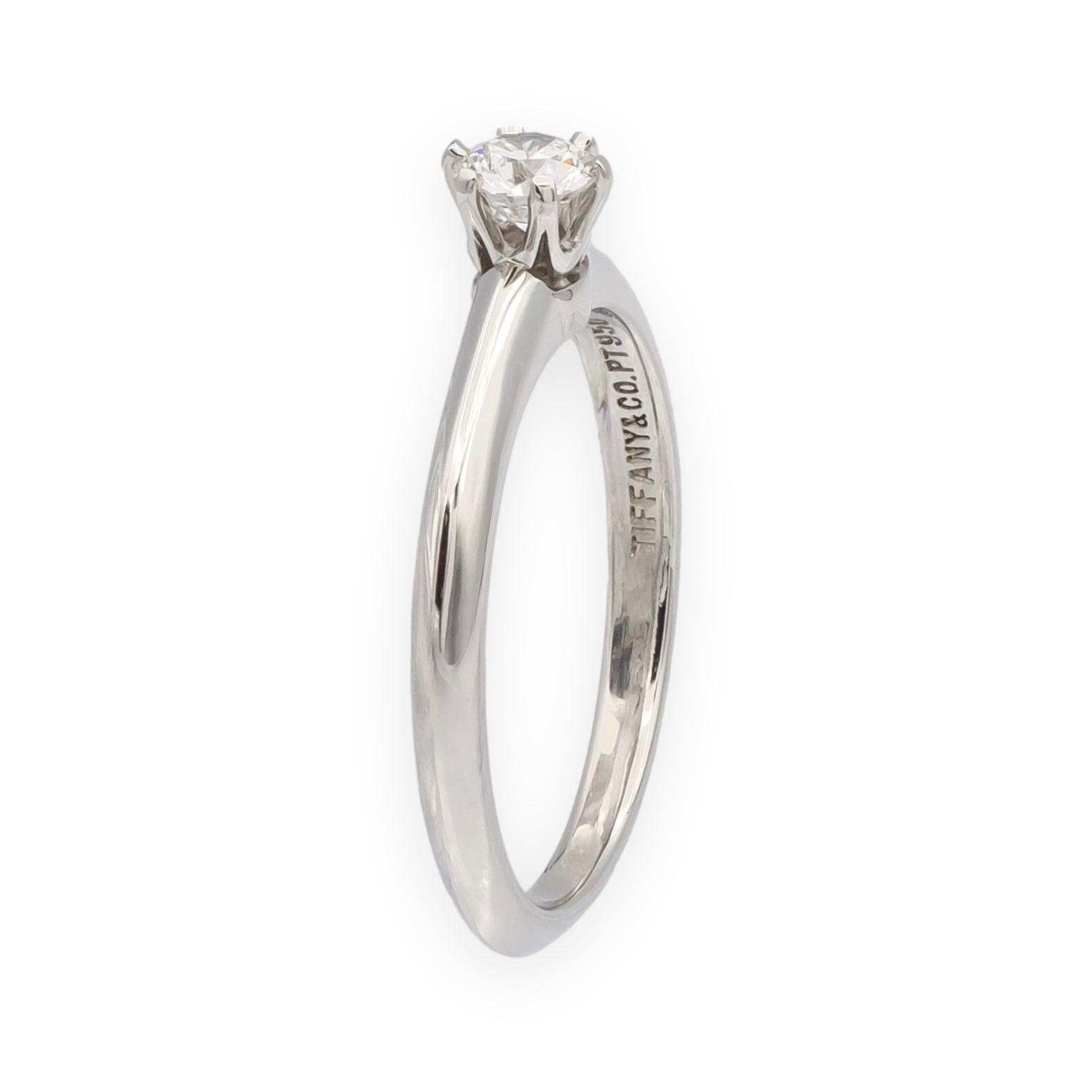 Classico solitario a sei punte di Tiffany & Co. in platino, con incastonato un diamante tondo brillante da 0,22 carati di colore G e purezza VS2. L'anello presenta la tradizionale fascia Tiffany e un marchio che corrisponde al certificato incluso.