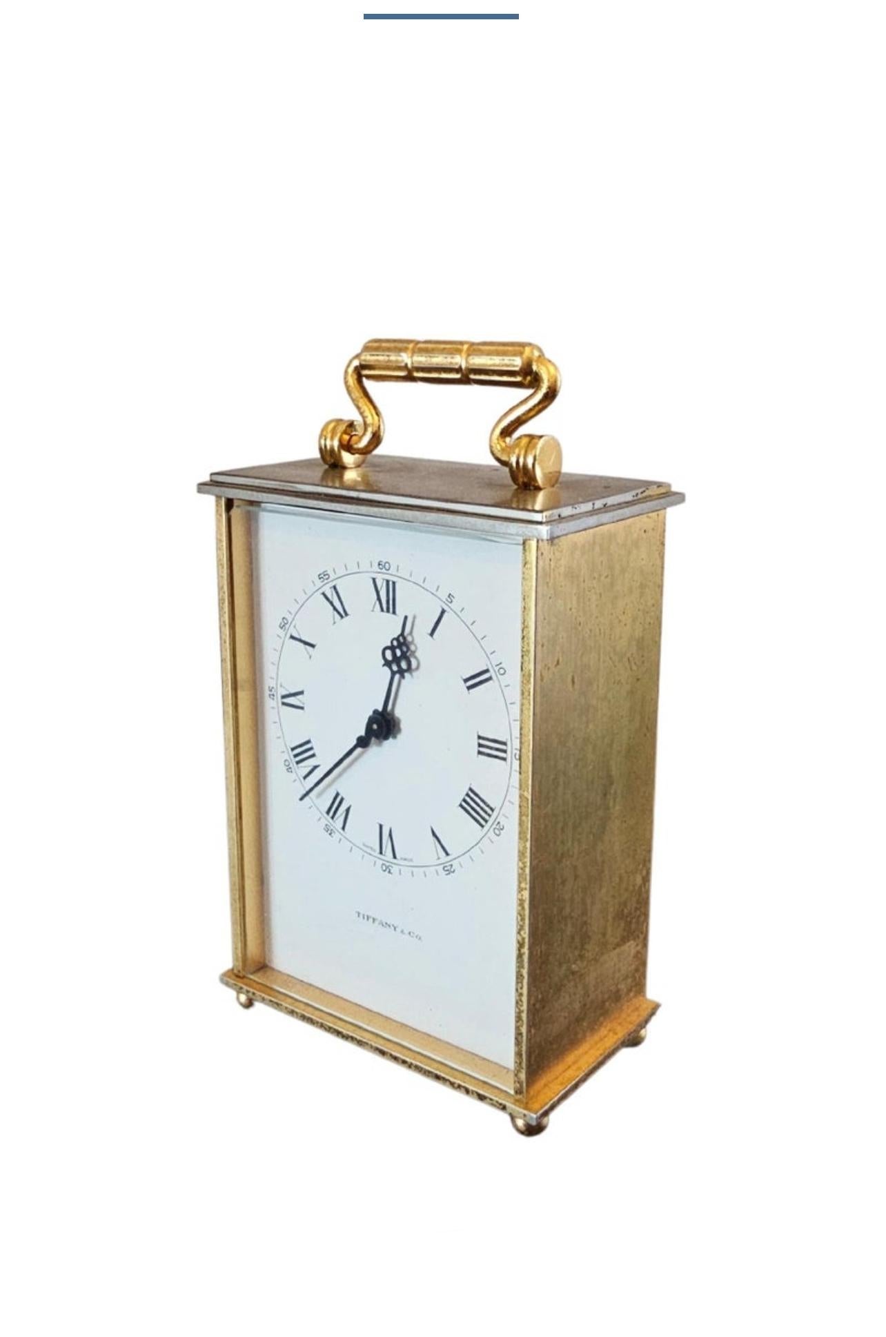 A vintage carriage clock retailed by luxury design house Tiffany & Co., mid-20th century, having a patinated gilt brass case with hinged carry handle, white enamel dial signed TIFFANY & Co., high-quality quality Swiss made 8-day 15 jewel movement,