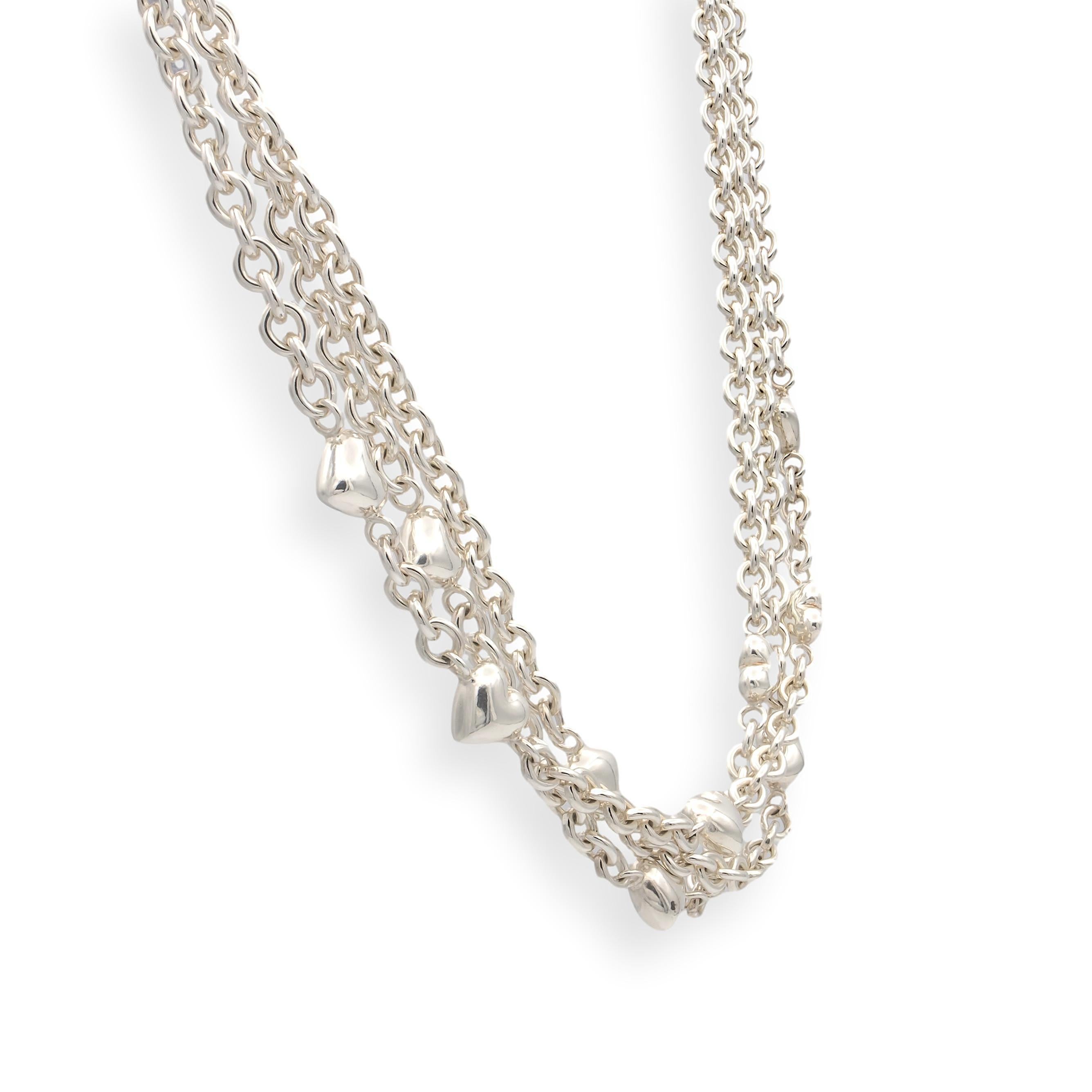 This vintage Tiffany & Co. necklace features three strands of sterling silver chain adorned with 10 puffed heart charms. The necklace measures 17 inches in length and secures with a toggle clasp. The puffed hearts measure approximately 10.5 x 11 mm