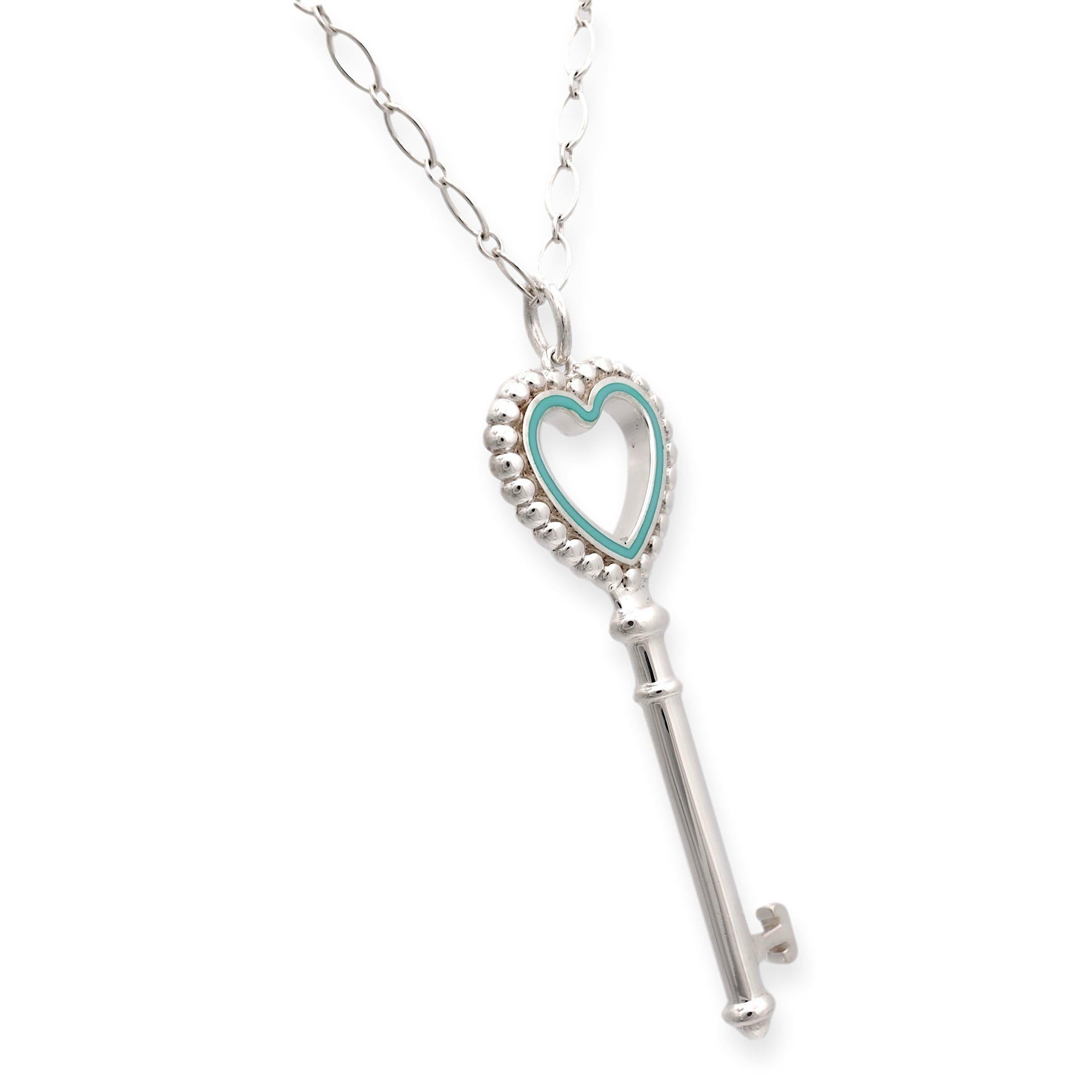 Tiffany & Co. Heart Key Pendant. Crafted with precision in sterling silver and adorned with a delicate blue enamel border around the heart, dangling gracefully from a 30-inch oval link necklace, fastened with a secure spring ring closure. The