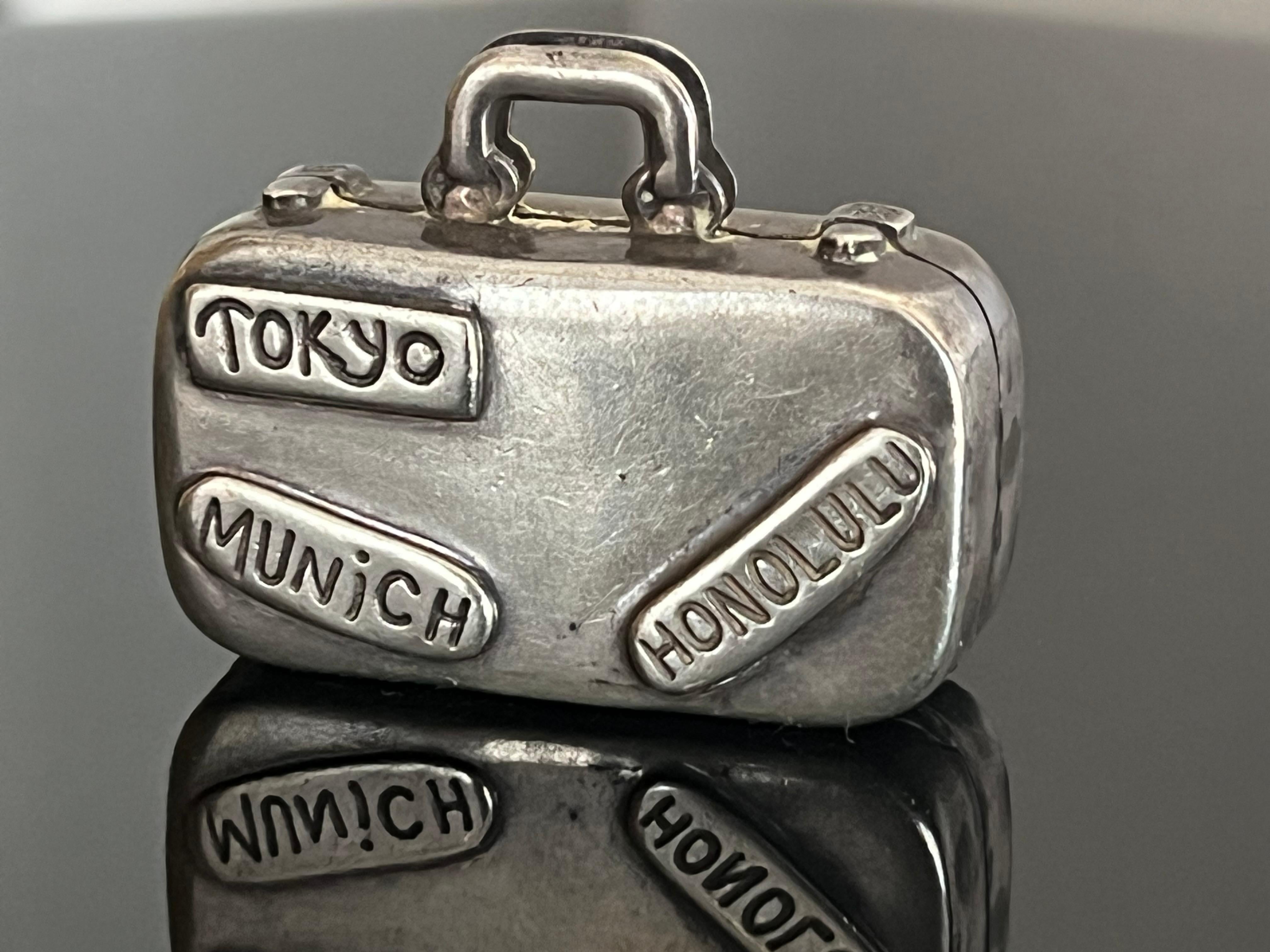 Charming, vintage pill box by Tiffany & Co. Rare and out of production miniature box in the shape of a suitcase. One side bears tags that say TOKYO, MUNICH and HONOLULU, the other side bears tags that say LONDON, BEVERLY HILLS and NEW YORK. T&CO 925
