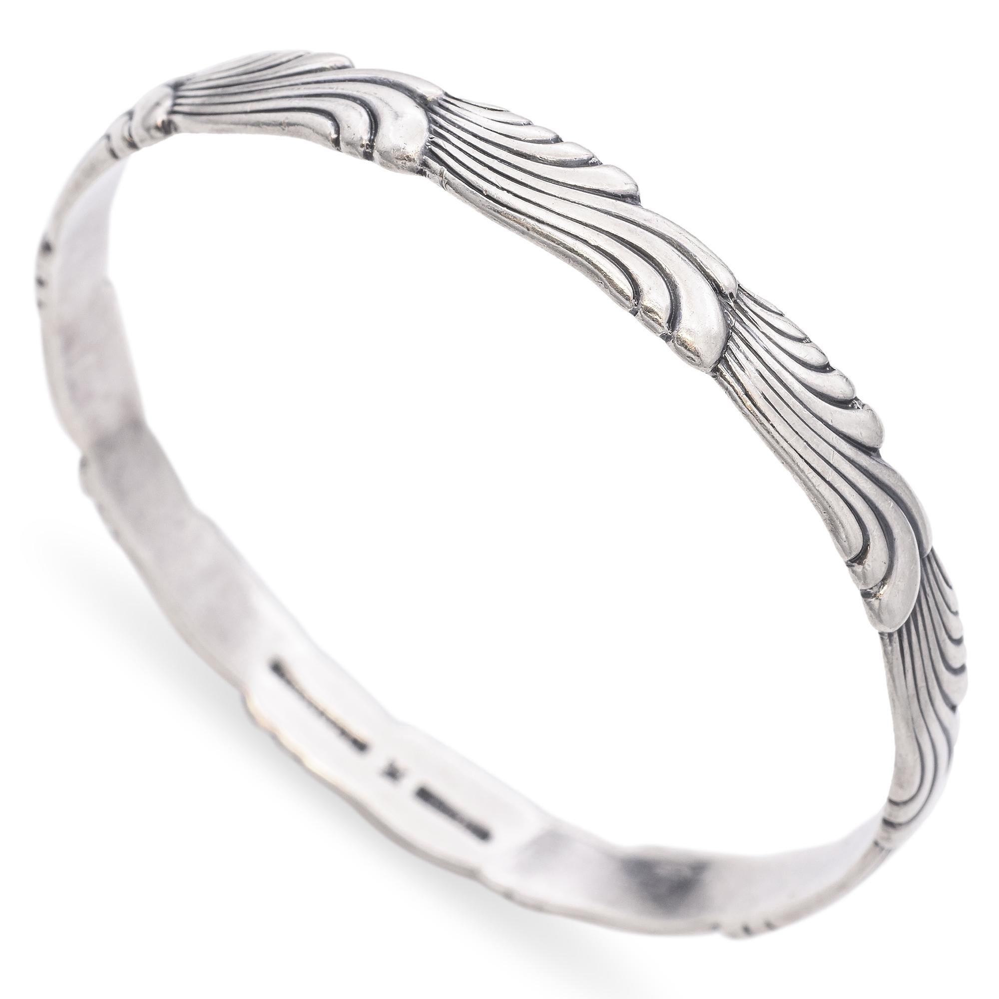 Questo braccialetto bangle in argento sterling di Tiffany & Co. presenta un intricato disegno a onde inciso sulla superficie. Il delicato motivo è sottile ed elegante e mette in mostra la rinomata abilità artigianale del marchio. Un pezzo senza