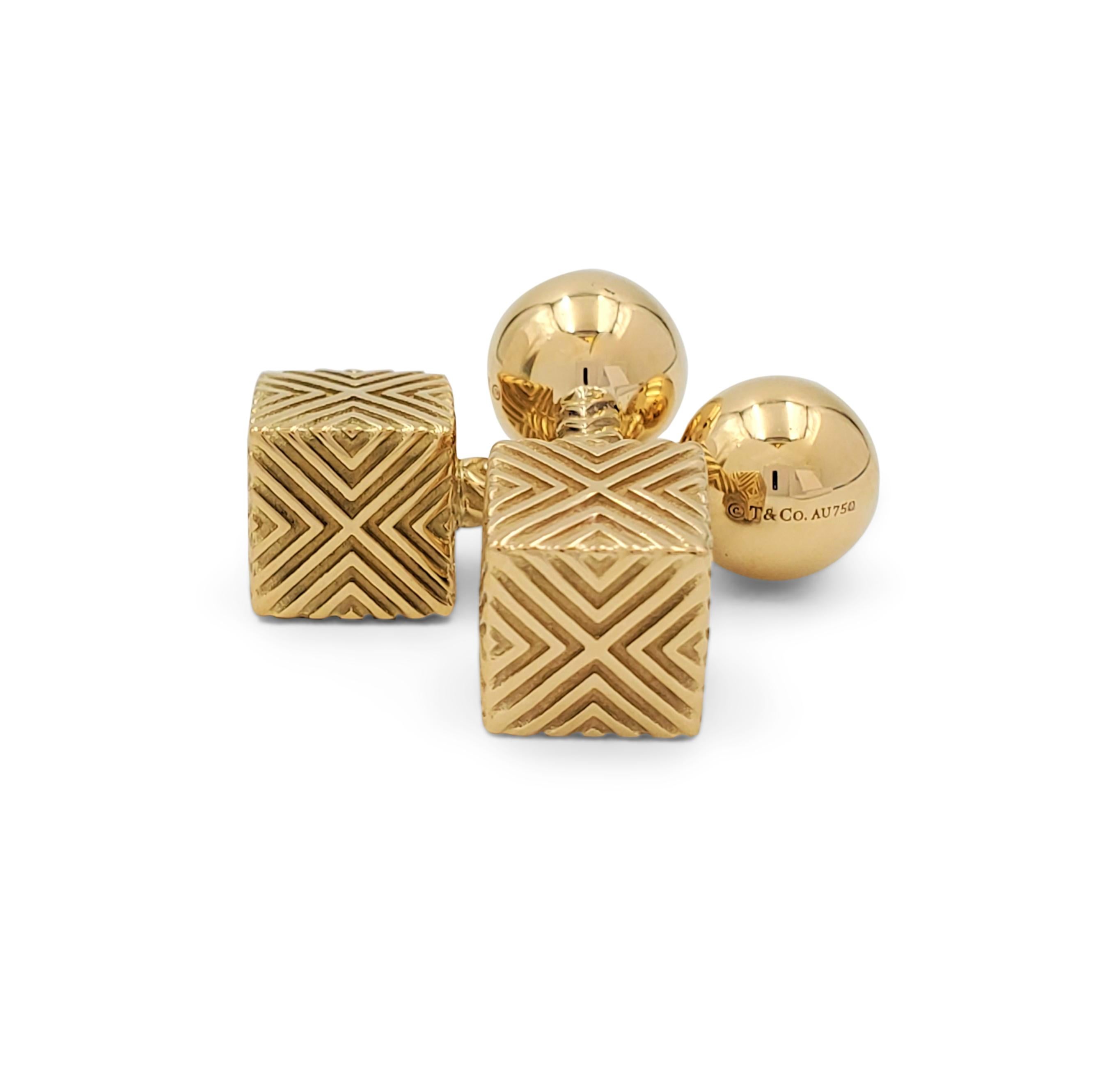 Authentic Tiffany & Co. cufflink pair crafted in 18 karat yellow gold. One end of the cufflink centers on a round high polished gold ball with the Tiffany & Co. signature and a 750 Au gold stamp. The other end of the cufflink is a gold cube with 'X'