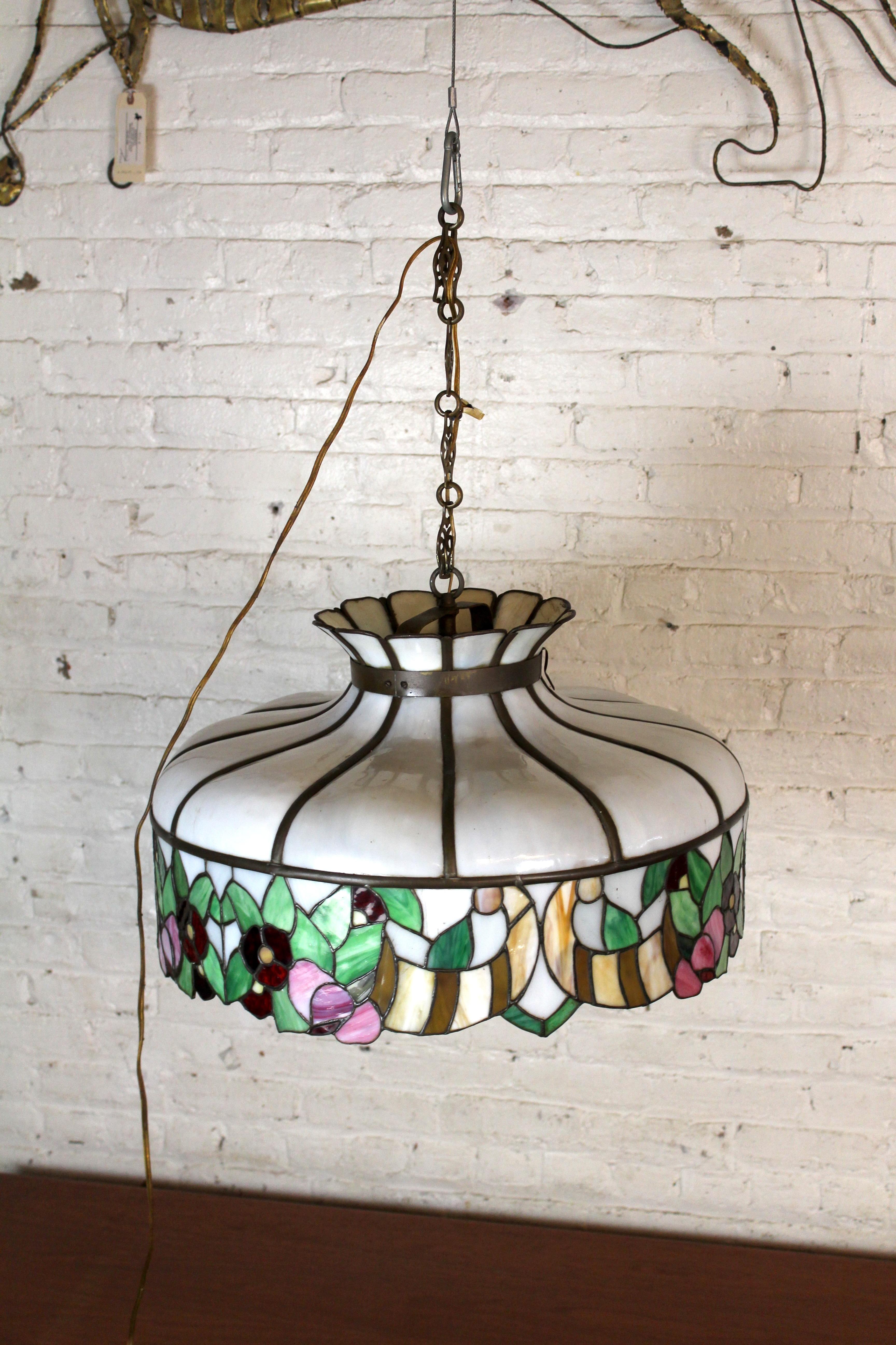 Colorato e decorato, questo lampadario vintage in stile Tiffany presenta uno splendido paralume in vetro colorato composto da vibranti vetri piombati con motivi floreali e geometrici. Quando è illuminato, proietta una luce calda e ambientale,