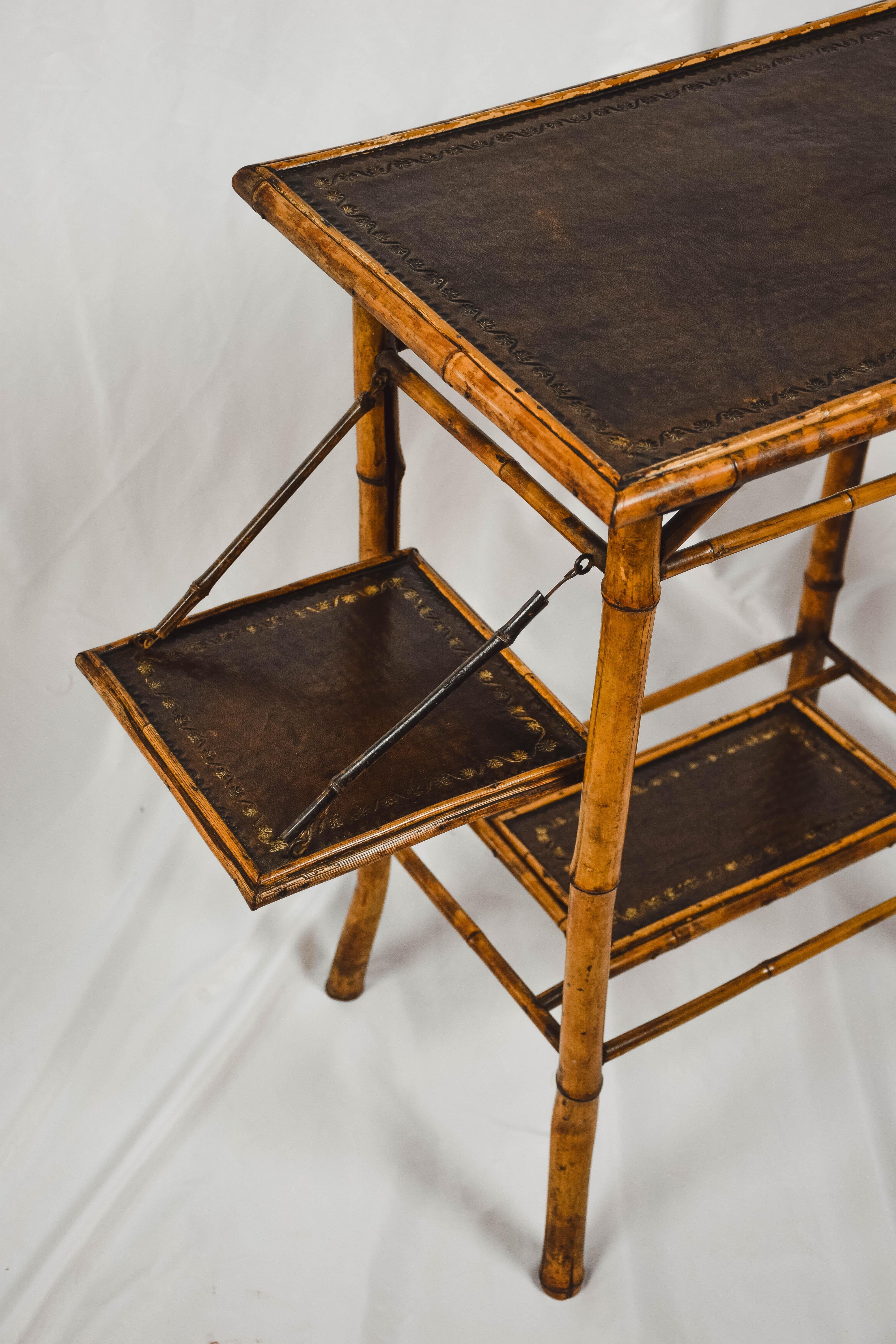 Vintage two tiered tiger bamboo small table with leather embossed top and shelf. The piece also has two leather embossed side shelves that fold up and down.