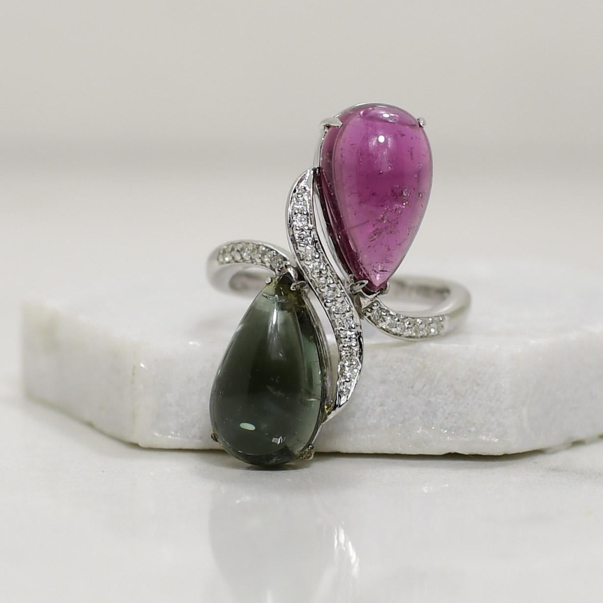 This exquisite 14K vintage white gold ring captures timeless elegance with its enchanting design. The centerpiece features a lustrous pear-shaped cabochon cut gemstone, combining rich green and regal purple hues, creating a captivating play of
