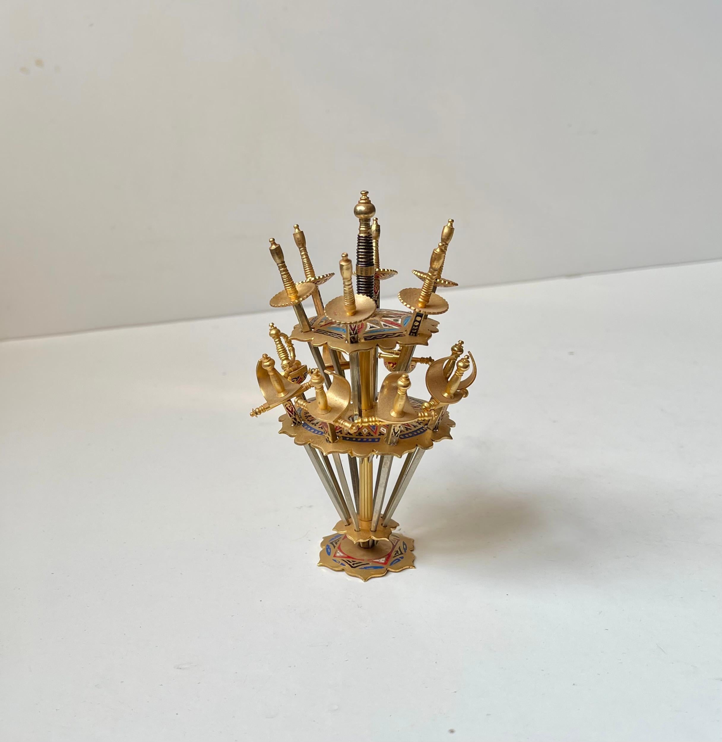 A Spanish Souvenir or novelty item from the 1970s in the shape of this sword skewer set. 15 swords in a matching stand. Made from steel, brass and enamel. Suitable for cocktails, olive snacks etc. Made in Toledo Spain. Measurements: swords: 8.5 cm