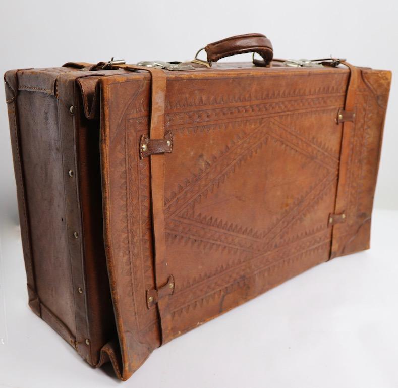 Stylish vintage luggage suitcase in weathered leather. This suitcase has a hand tooled surface, and floral print fabric interior. It shows signs of age band use, including tears to the strap loops, and general cosmetic wear, as shown. Usable as is