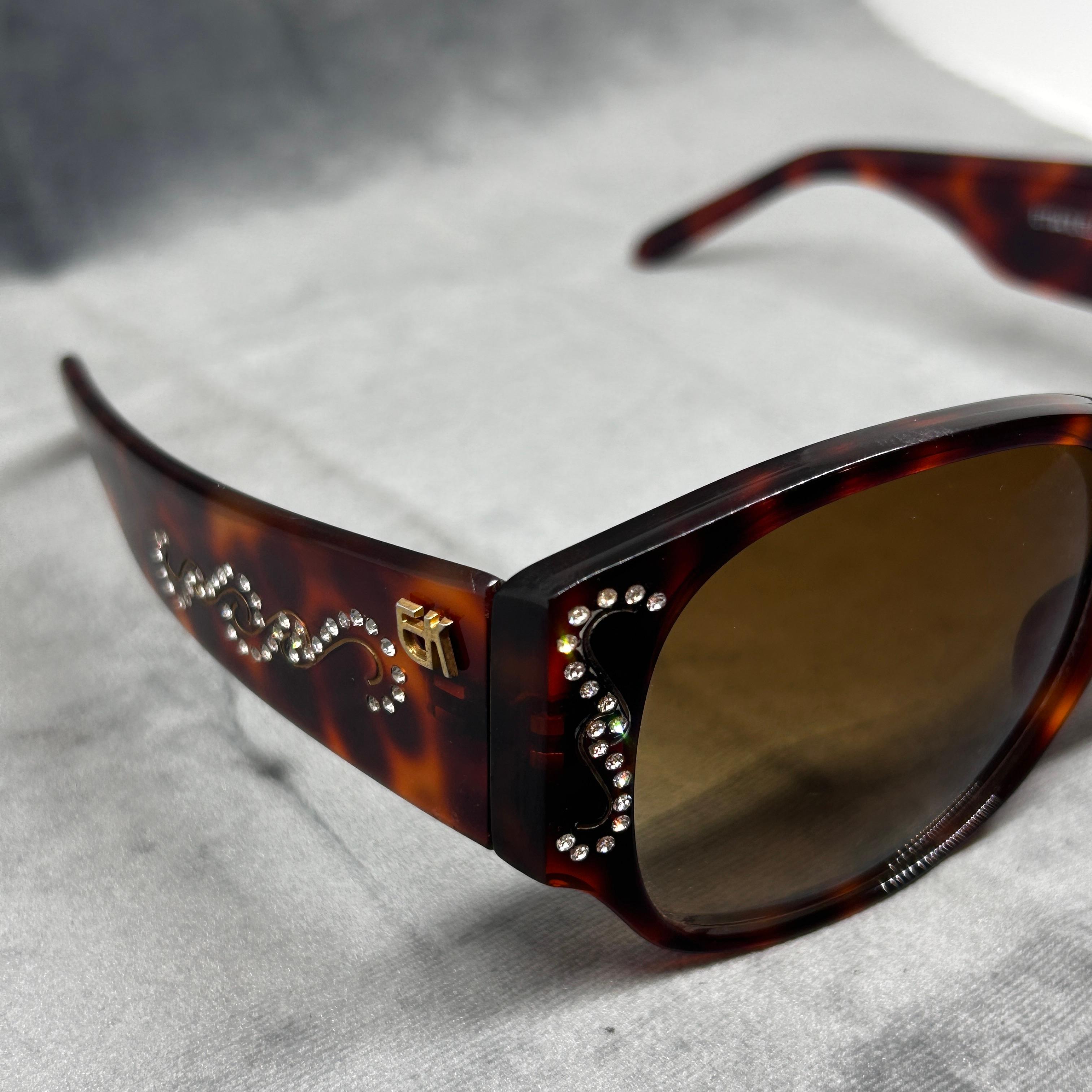 Die Sonnenbrille ist mit einem Schildpattmuster auf einem Lucite-Rahmen versehen. Das Design ist überdimensioniert, typisch für den Retrostil. An den oberen Rändern sind sie mit Strasssteinen verziert, die dem Look ein dekoratives und luxuriöses