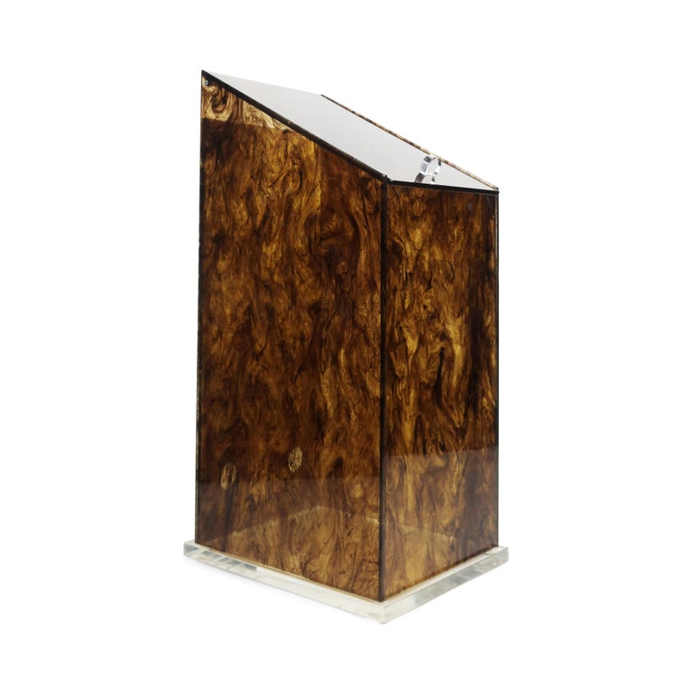 A vintage acrylic storage piece in faux tortoiseshell that captures all of the glamor of the Hollywood Regency style. Sitting on a square clear Lucite base, it has a sloped lid that opens with a clear Lucite pull. Vent holes on the rear suggest this