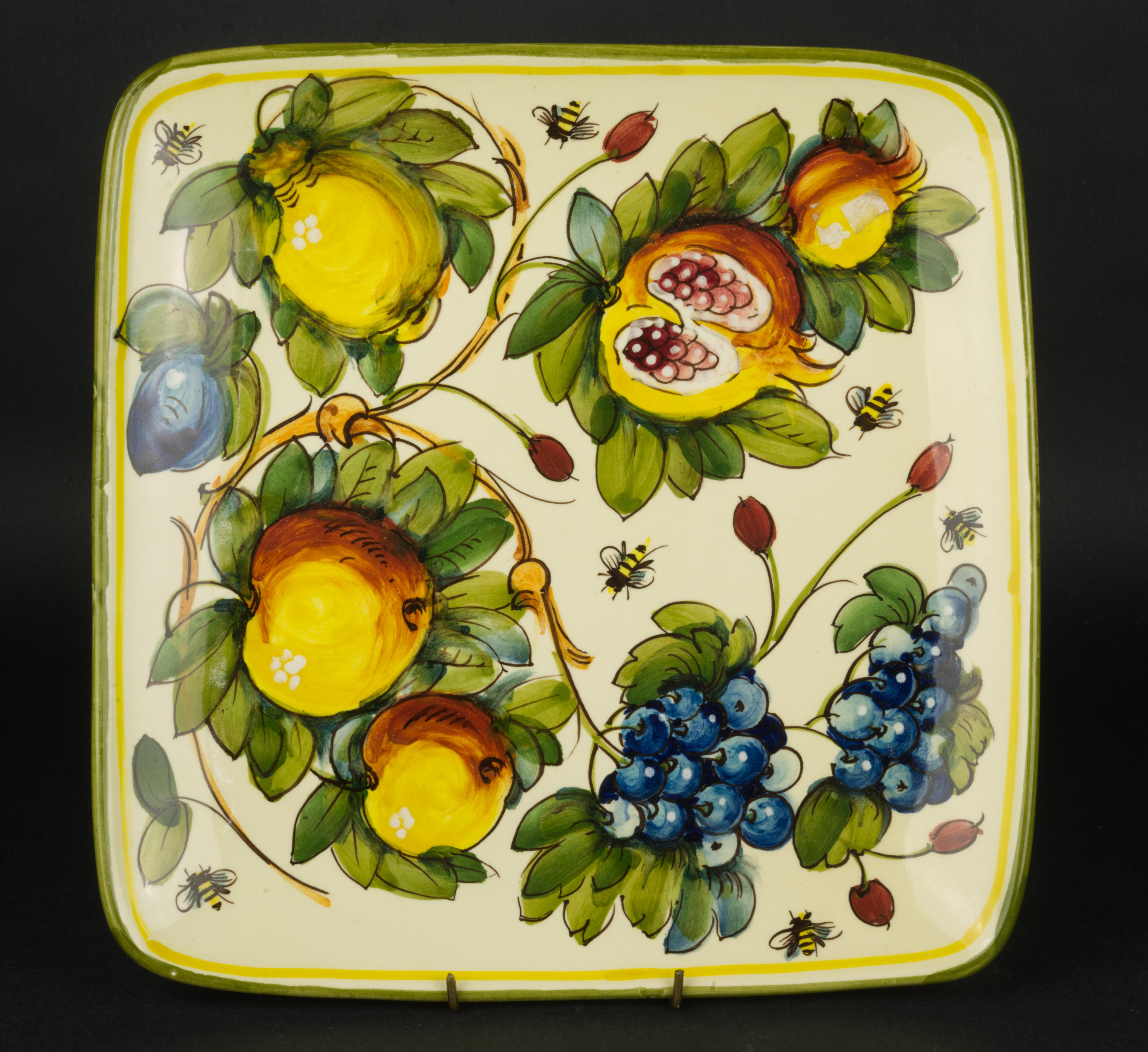  Le plat de service carré en majolique vintage a été fait et peint à la main dans la région de Toscane en Italie. Le motif Toscana Bees présente divers fruits sur un fond jaune chaud, avec des bourdons qui volent autour. Le bord vert olive chaud est