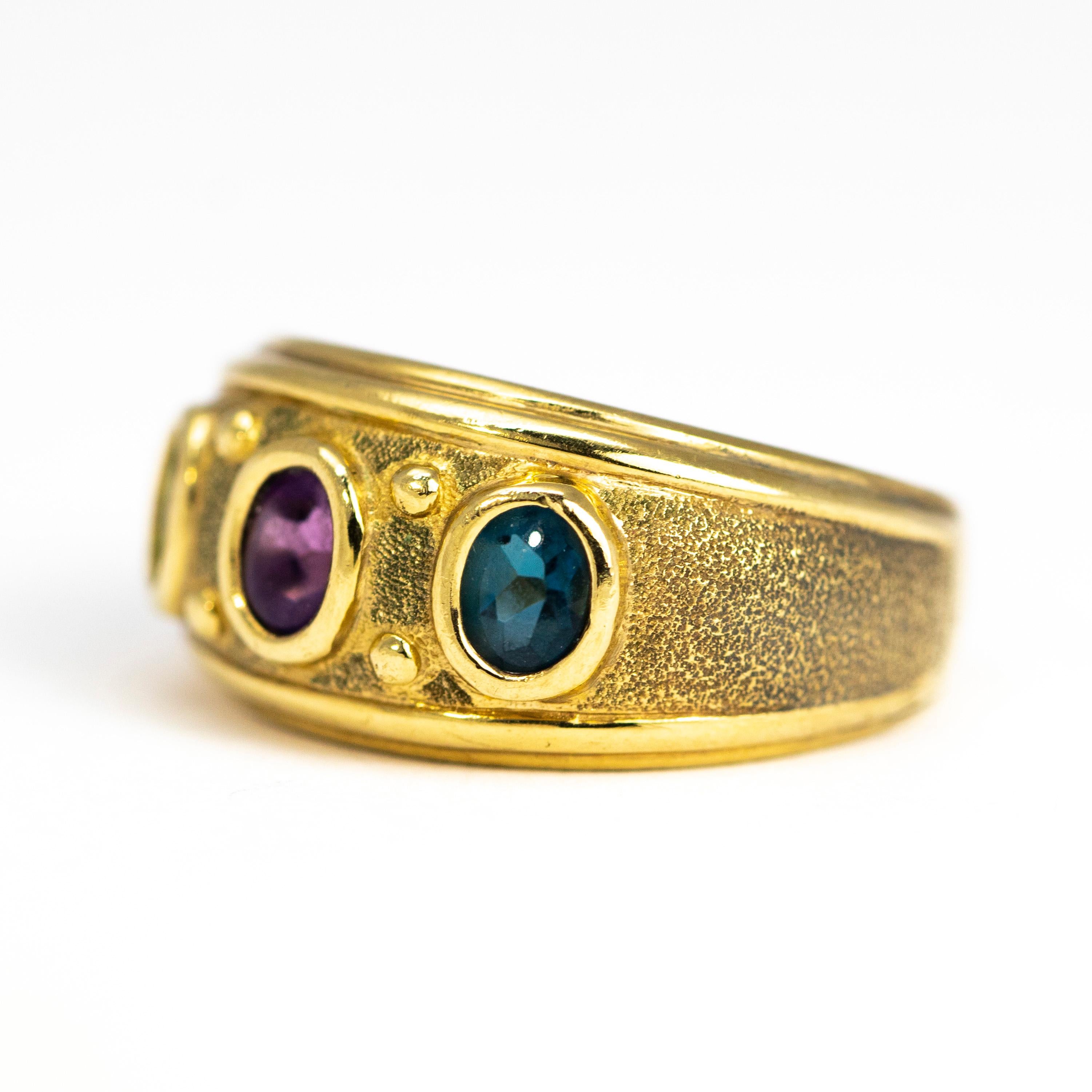 This stylish and chunky band ring holds three different coloured tourmaline stones measuring 40pts each. The stones are striking blue, deep purple and bright green. Surrounding the stone is textured gold and the outer edges are smooth and glossy.