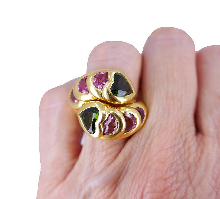 A colorful tourmaline ring made of 18k yellow gold.
It’s a vintage bypass ring with two heart-shaped green tourmalines and six halfmoon-shaped pink tourmalines. The ring has a snake design, with the pink gemstones set in the gold coils reminiscent