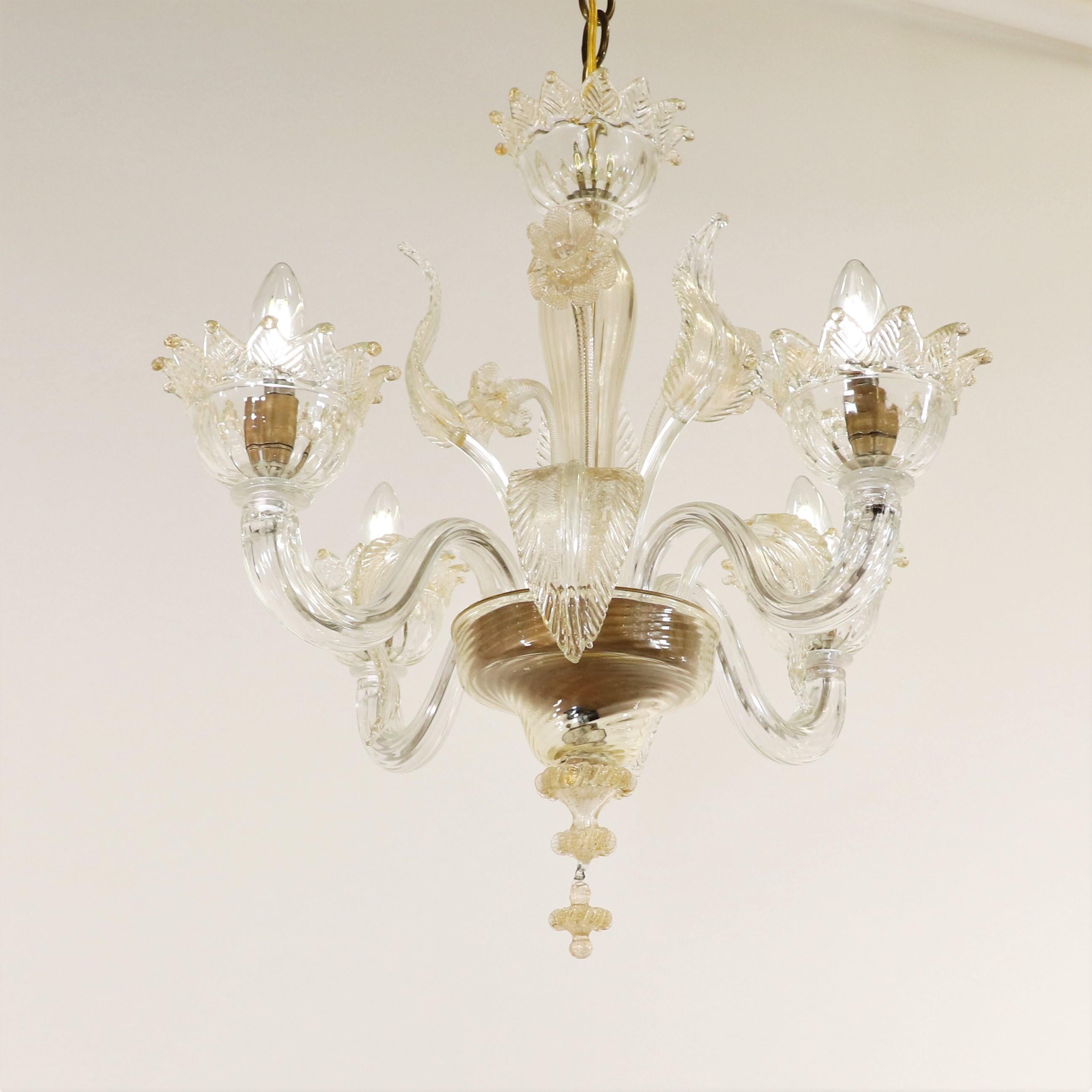 Questo lampadario floreale in Cristallo di Murano, realizzato a mano e infuso in oro, presenta quattro bracci a voluta che sorreggono bobeches con finiture a foglia. Il lampadario vanta una colonna centrale a bulbo ornata da dettagli fioriti,