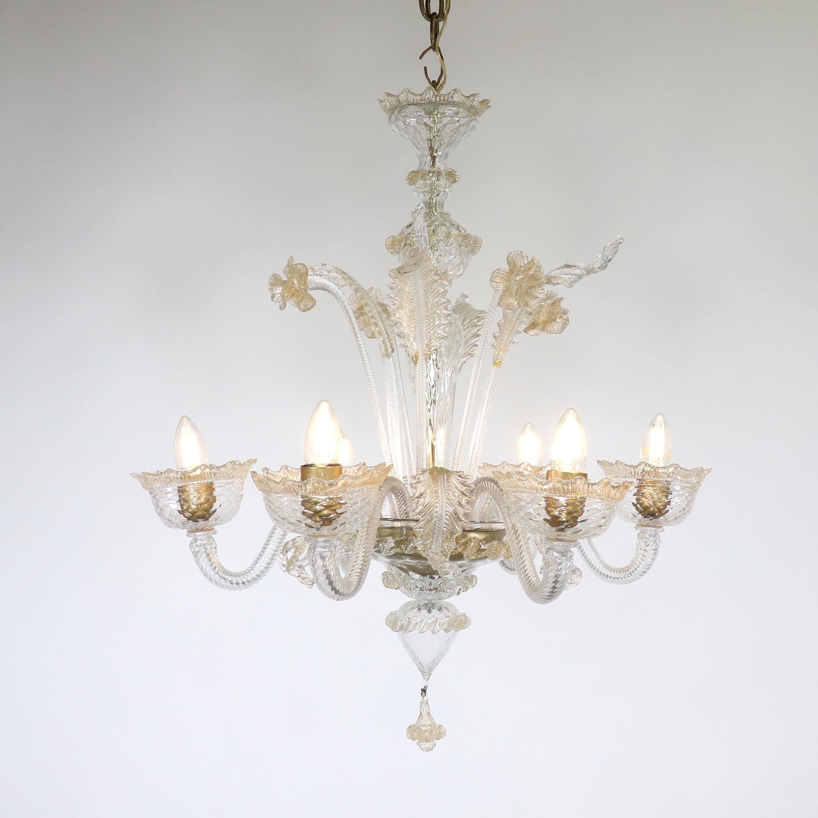 Questo lampadario floreale di Murano, realizzato a mano e infuso in oro, è caratterizzato da sei bracci a voluta ondulati che sorreggono bobeches con struttura a reticolo e finiture a foglia. La colonna centrale a bulbo è ornata da dettagli fioriti,