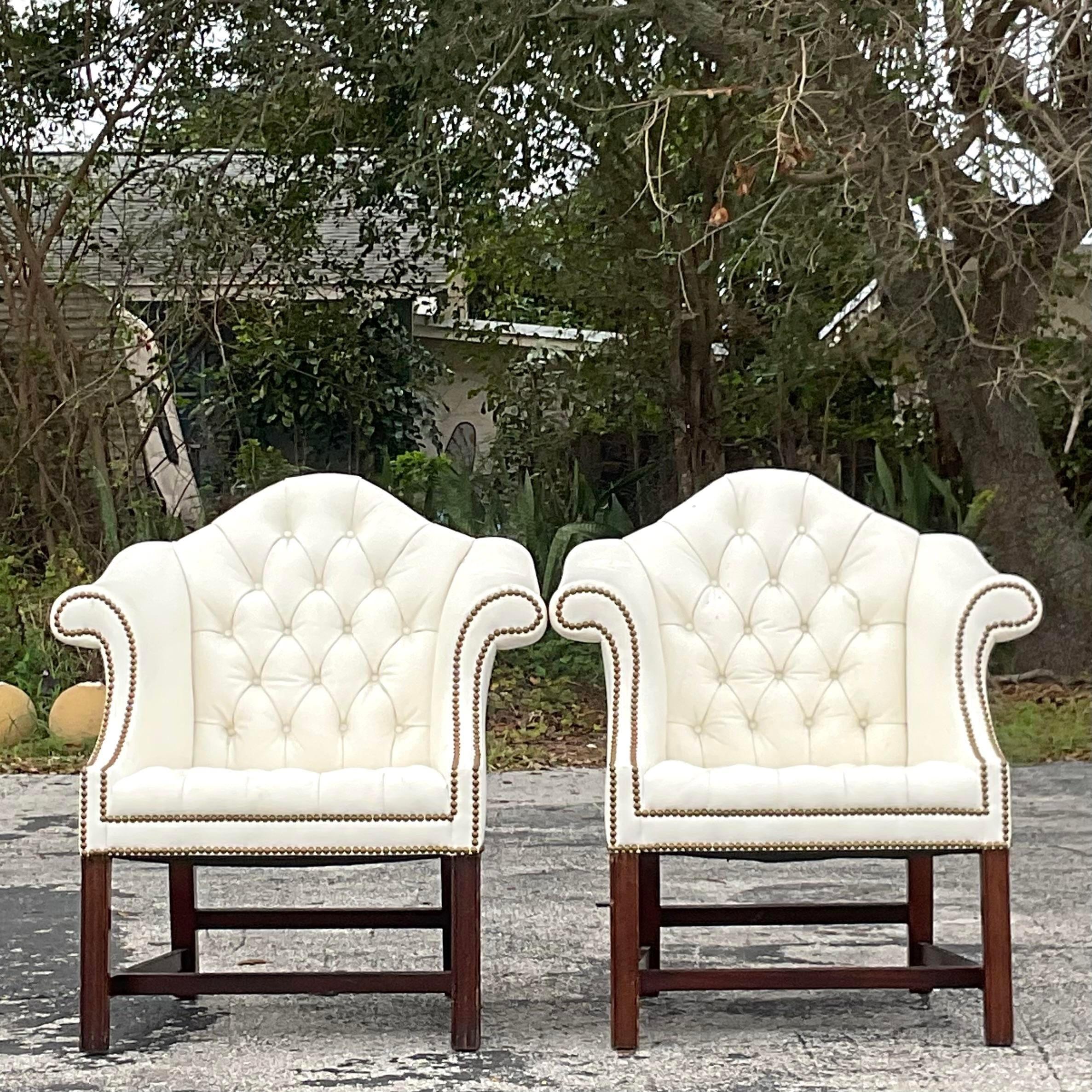 A fabulous pair of vintage traditional arm chairs. A chic camel back shape in a white tufted leather. Burnished brass nailhead trim. Acquired from a Palm Beach estate.