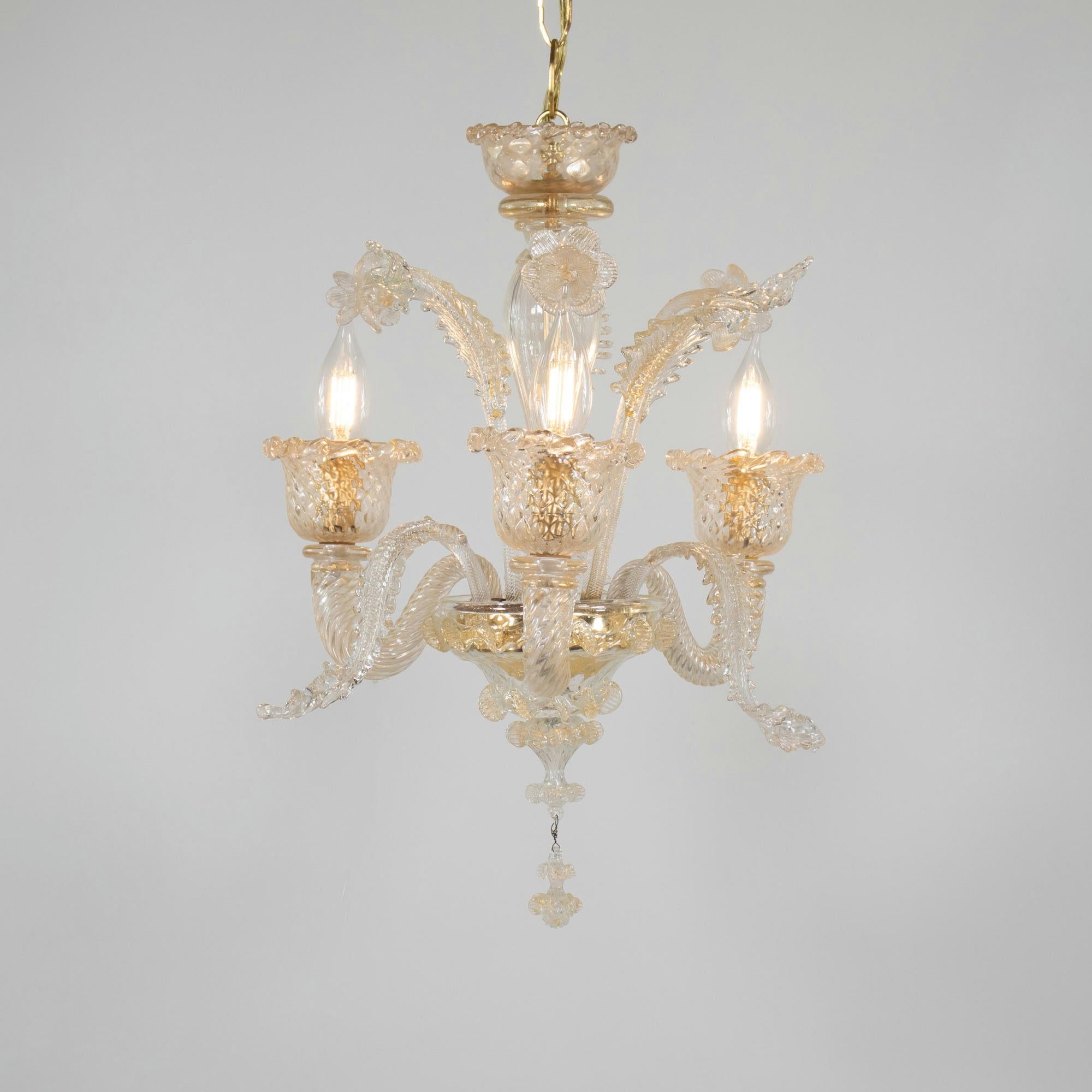 This vintage handcrafted gold-infused cristallo Murano chandelier has three scroll arms with chalice cups, utilizing a rigaree trim. Featuring a bulbous center column with blooming details, stylized here with daffodils and leaves. Despite its small