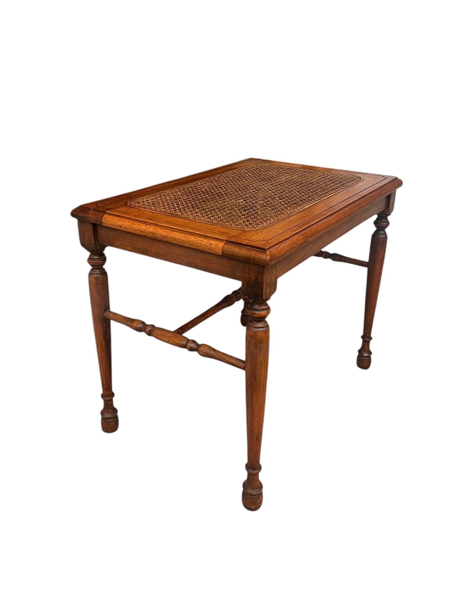 La panca decorativa in legno vintage presenta un design classico con una finitura ricca e lucida che mette in risalto le venature naturali del legno. Il suo piano rettangolare è impreziosito da un intarsio di canne intrecciate che aggiunge un tocco