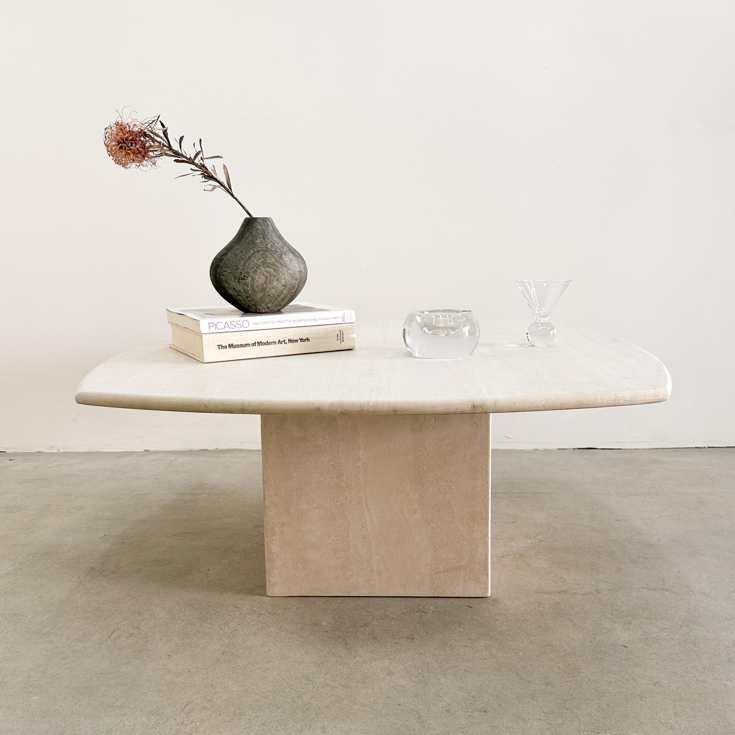 This vintage 1980s travertine coffee table features a solid stone construction with a smooth rounded edge for a sleek, sophisticated look. Designed in two pieces, the sturdy square tabletop rests securely on its matching base, creating a timeless