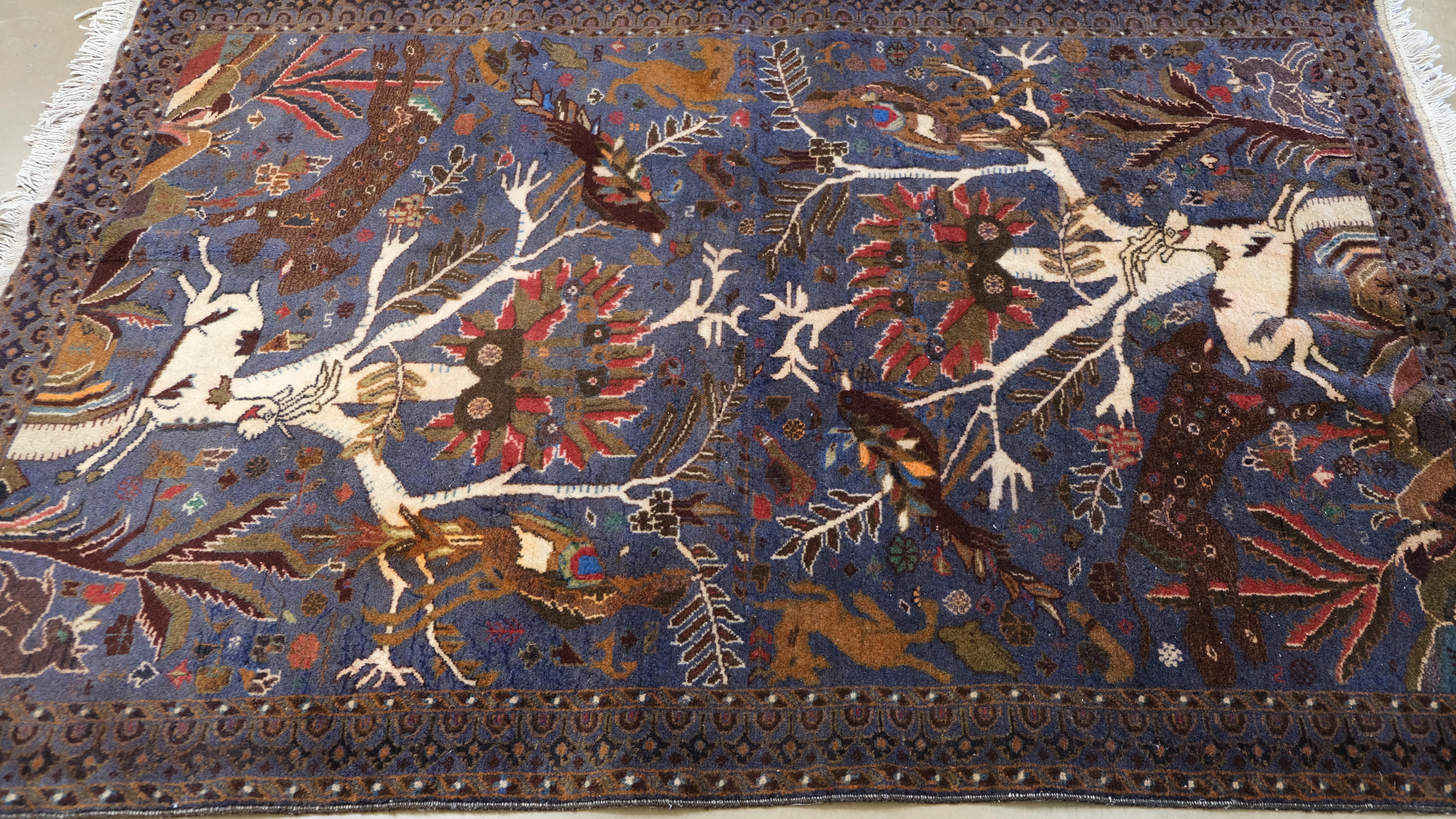 This exquisite hand-knotted wool rug is a striking example of tribal artistry, featuring an intricate hunting scene set against a deep field. Woven by skilled artisans, the design depicts a dynamic tableau of animals, birds, trees, and abstract
