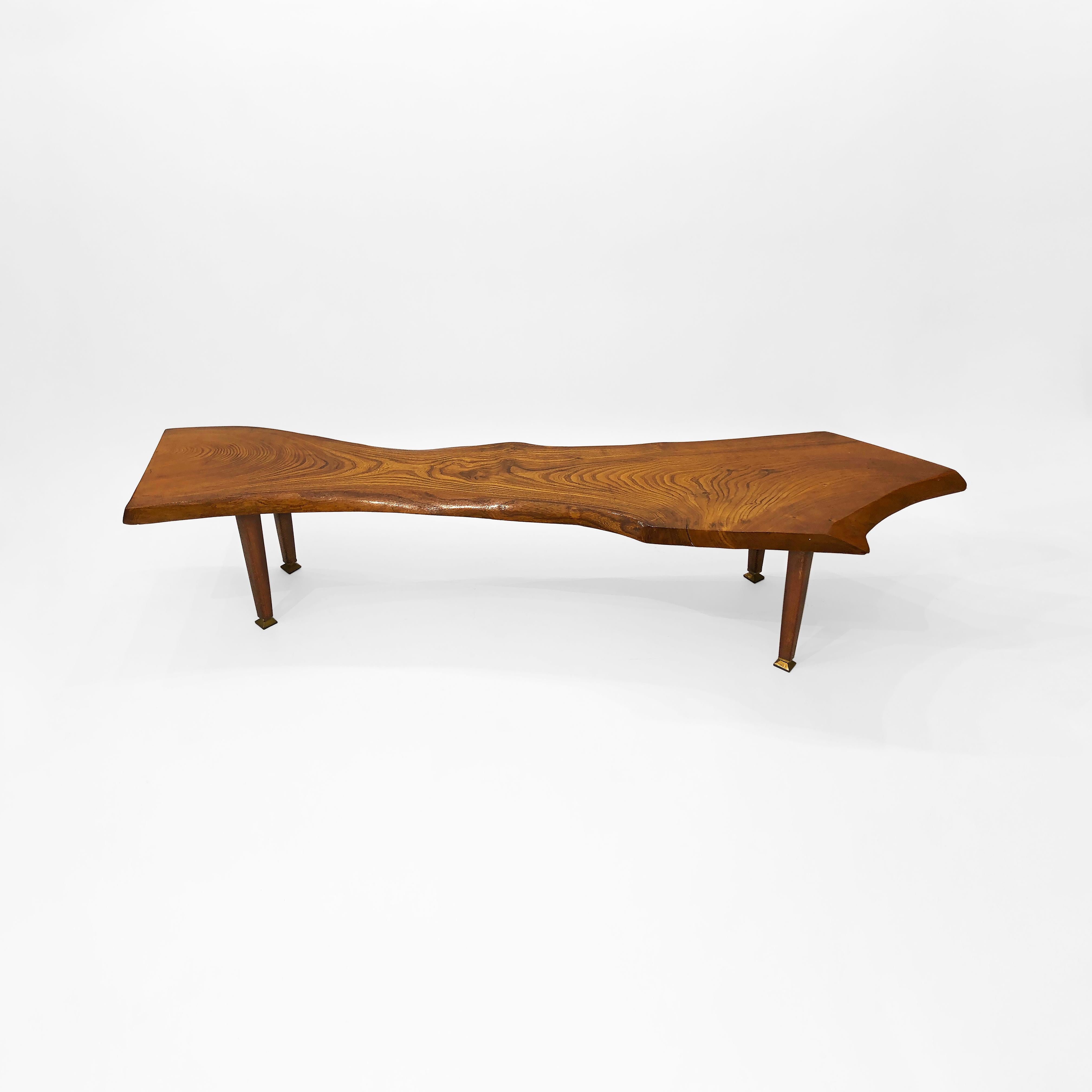 A tree trunk coffee table in organic form with beautiful wood grain and smooth texture. The tree trunk is cut straight on the one side and it takes an arrow shape with a pointed end on the other side. The wood grain meets in almost the middle giving