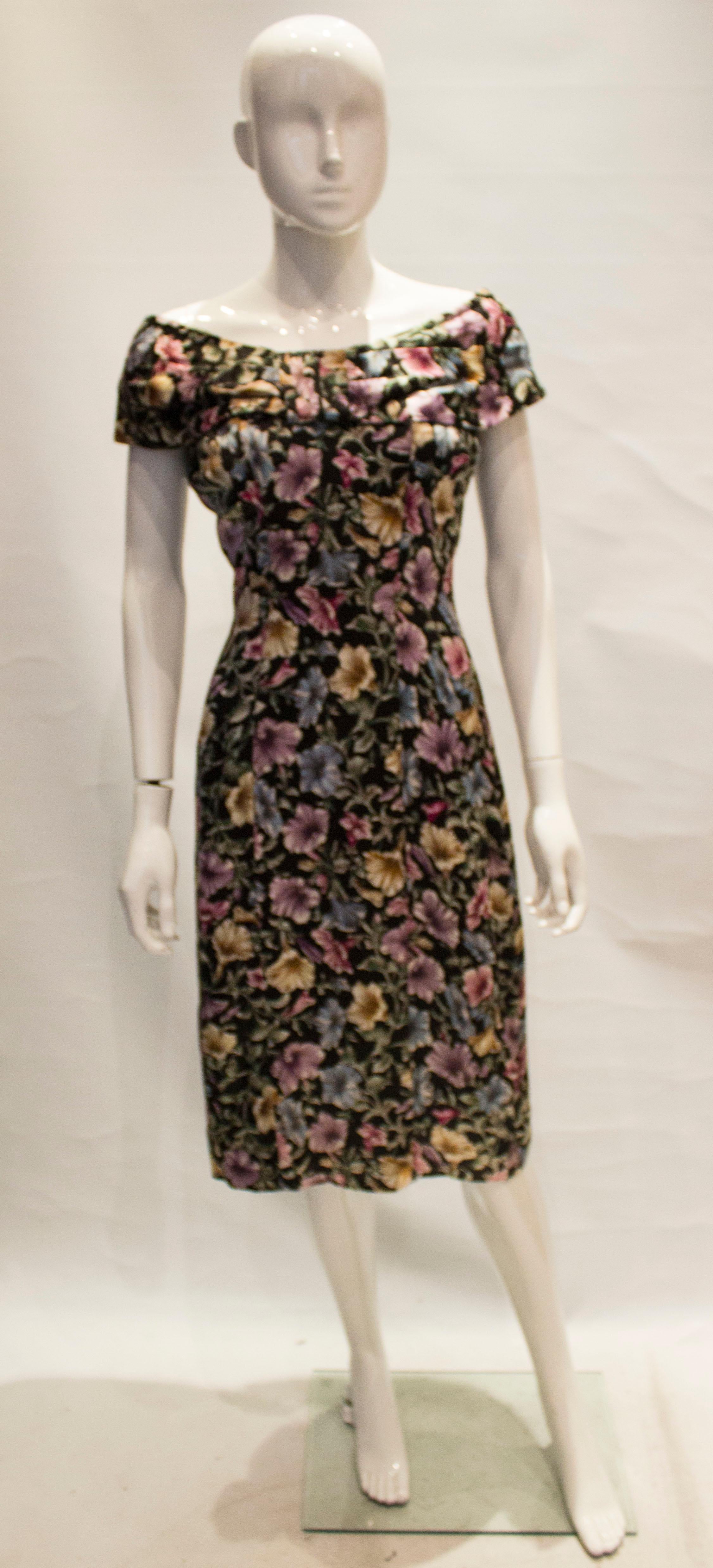  A pretty vintage cocktail dress by Tremara. The dress is off the shoulder with pleats around the neckline.The fabric has a black background with multicolour floral print. The dress has a 7 1/2 slit at the back and 2 1/2'' hem.