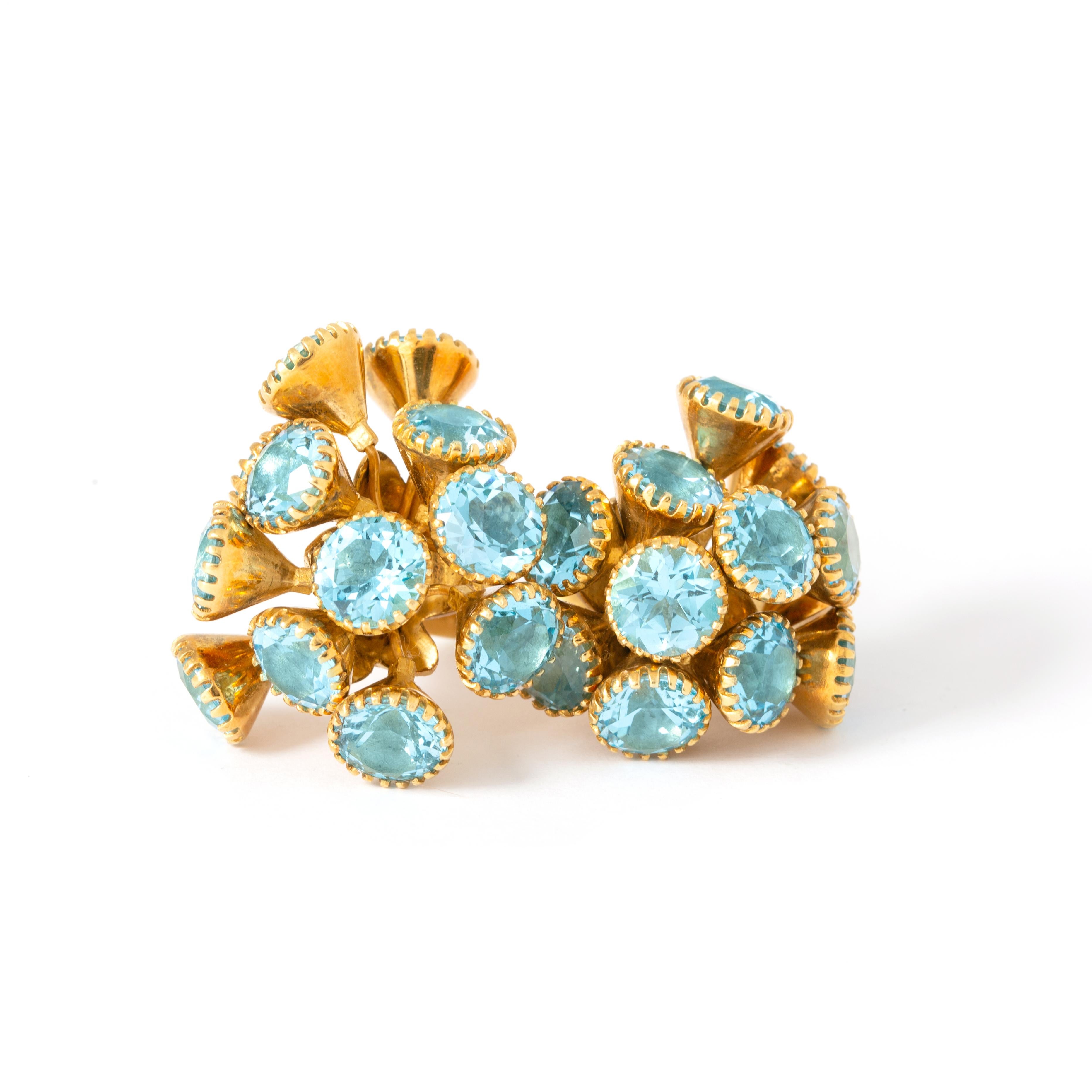 Statement ring features two clusters of round cut blue topaz 
Set in tapered flower-like forms that articulate
Completed by a wide and brightly polished shank with stylized floral shoulders
With maker's mark and tested as 18 karat gold
Ring Size: