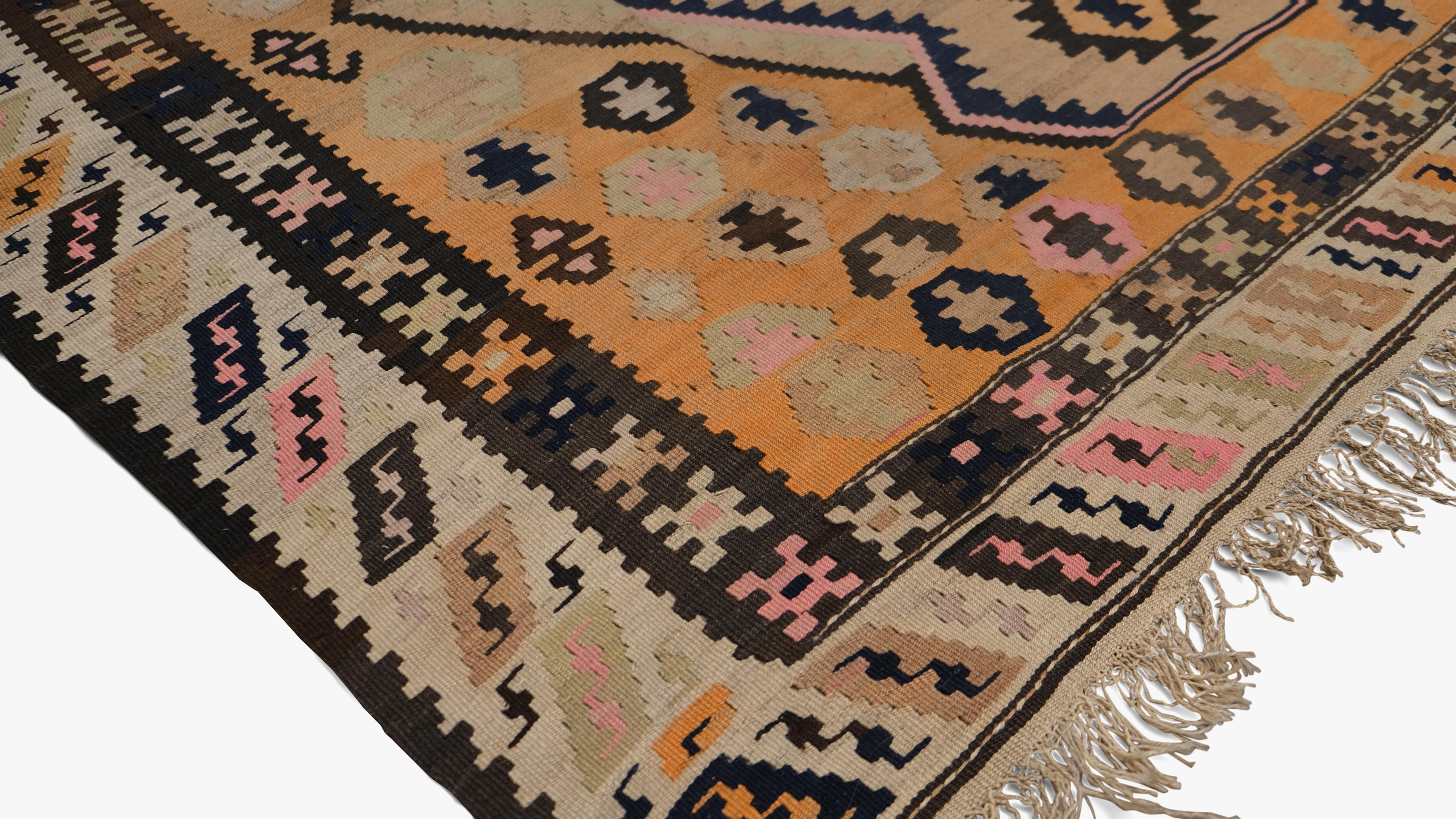 Este kilim de lana tejida a mano es una asombrosa representación de la artesanía tribal tradicional. La alfombra presenta un audaz dibujo geométrico de medallón en forma de diamante, enmarcado por intrincados motivos y símbolos que reflejan la rica