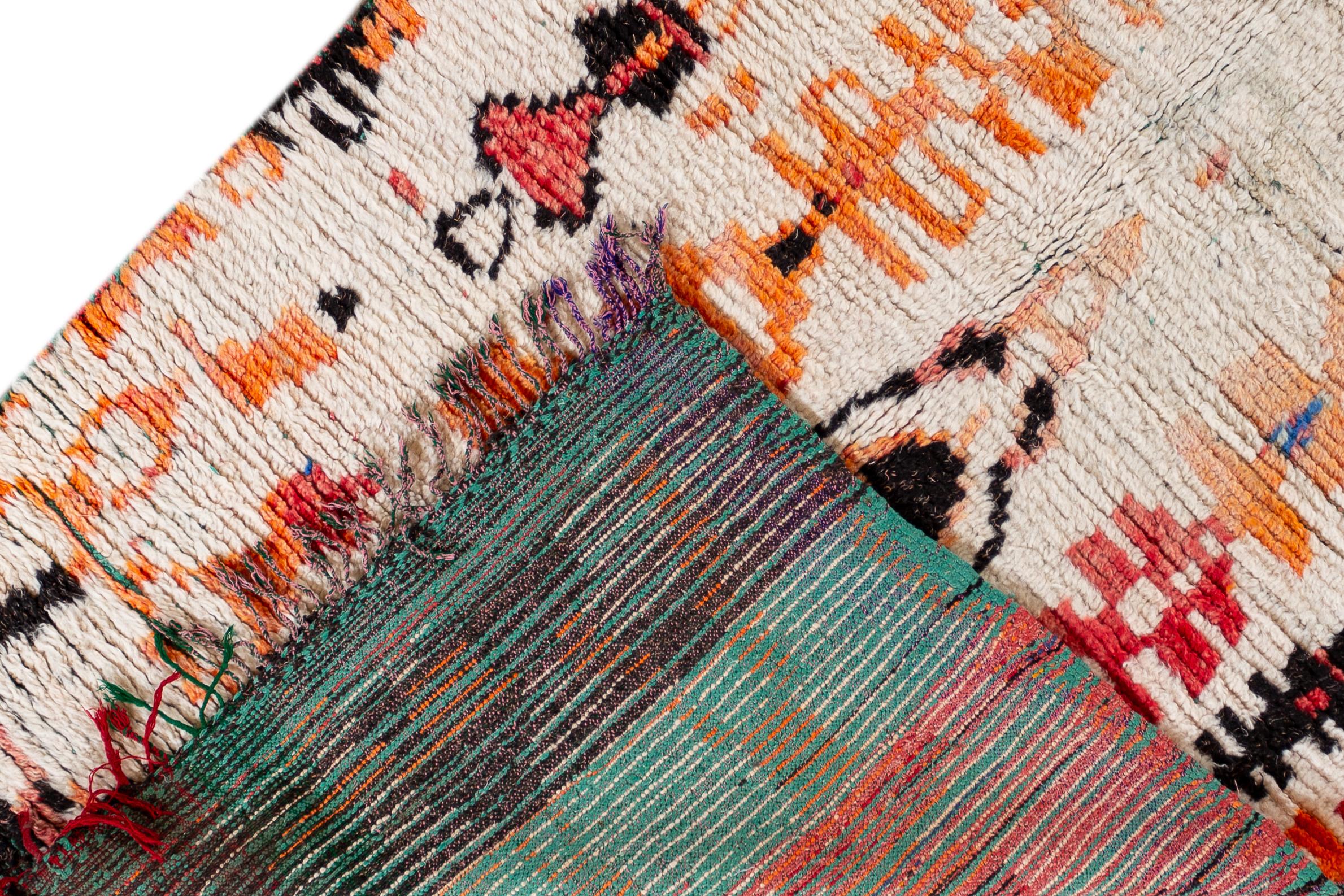 A vintage Moroccan rug with an ivory field and a vibrantly-colored tribal design of orange, red, blue and yellow. This hand knotted wool scatter rug measures 4'6
